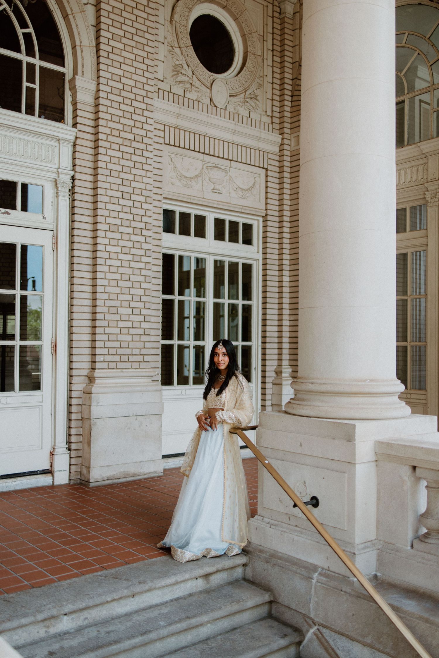 Bride in white gown enters elegant white brick building with classic columns and round window features.