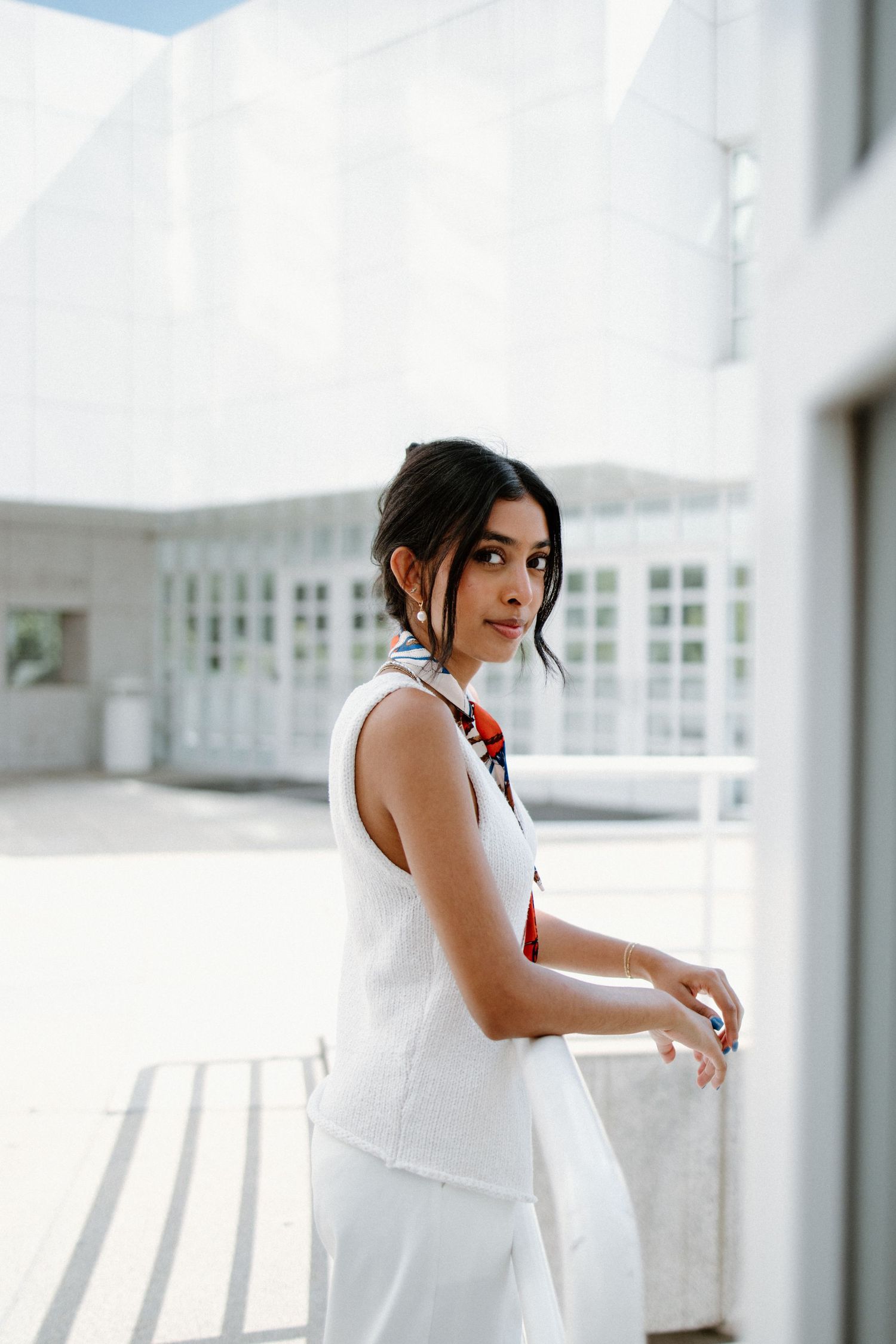Fashion portrait of woman in elegant white sleeveless dress standing in bright modern interior space.