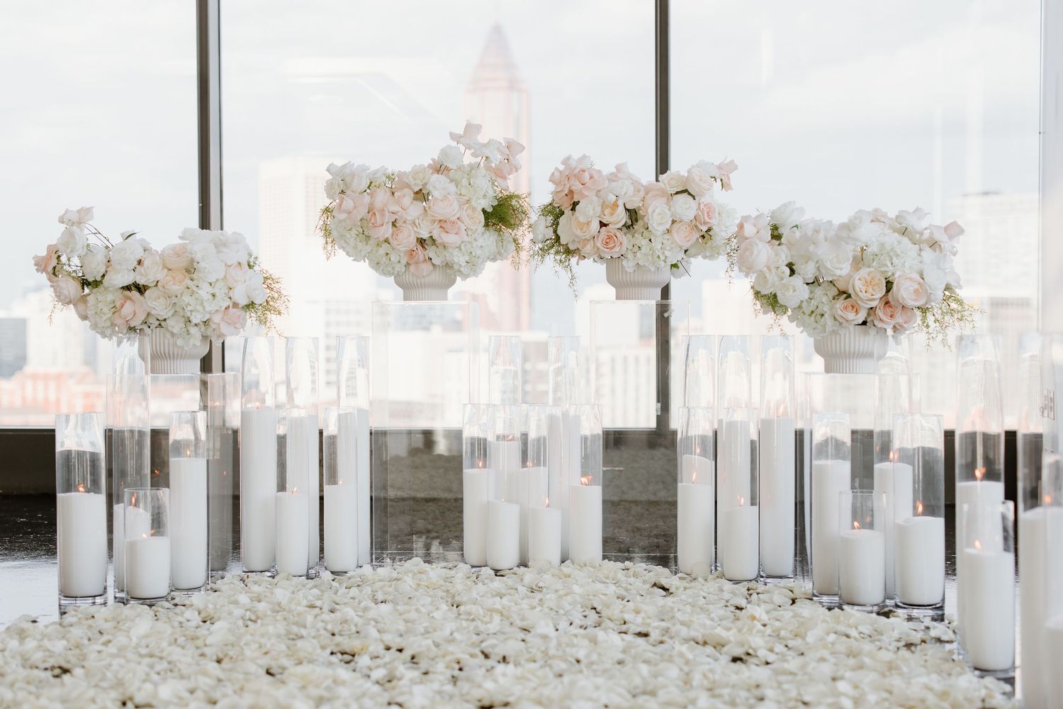 Elegant white and blush floral arrangements in tall glass vases surrounded by white pillar candles for wedding decor.