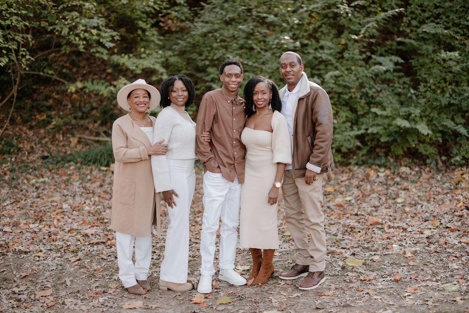 A group in coordinated cream and brown outfits poses together in a fall woodland setting.