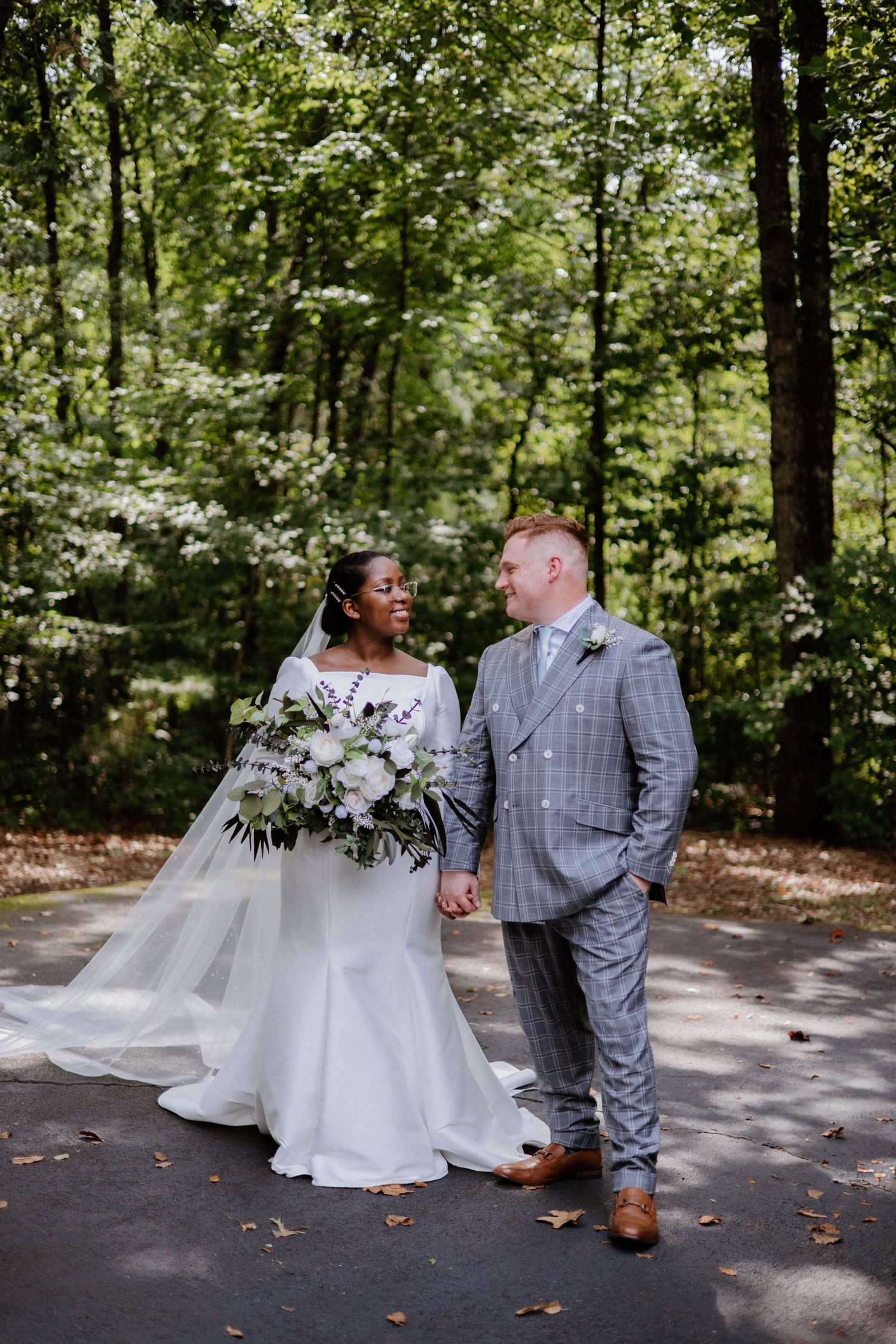 A couple in wedding attire shares romantic moments in different poses along a wooded pathway, surrounded by greenery.