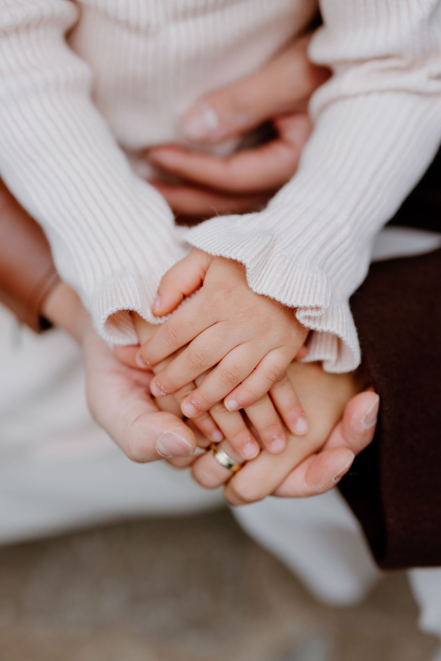 Hands wearing white sweaters hold each other tenderly while wearing a gold wedding band.