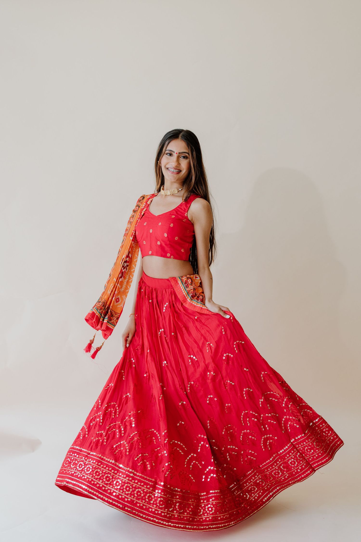 Traditional red lehenga with gold embroidery patterns and matching floral dupatta in Indo-Western fusion style against white background.