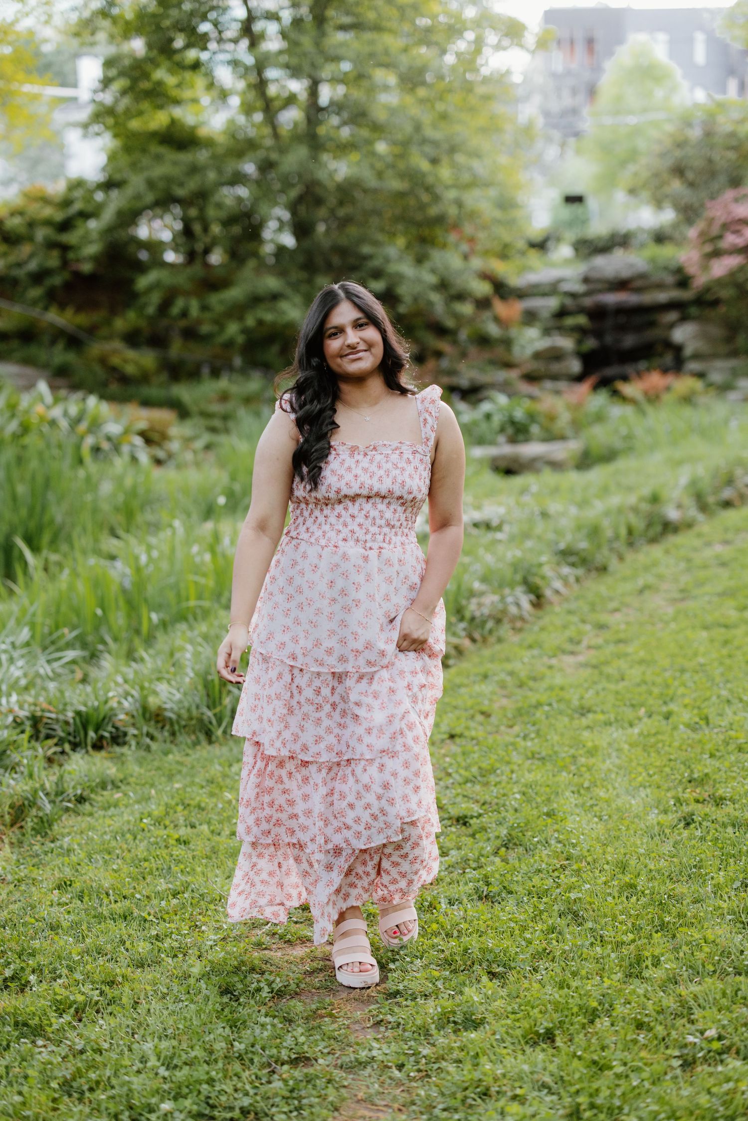 A person in a pink floral dress plays in a lush green garden setting on a summer day.