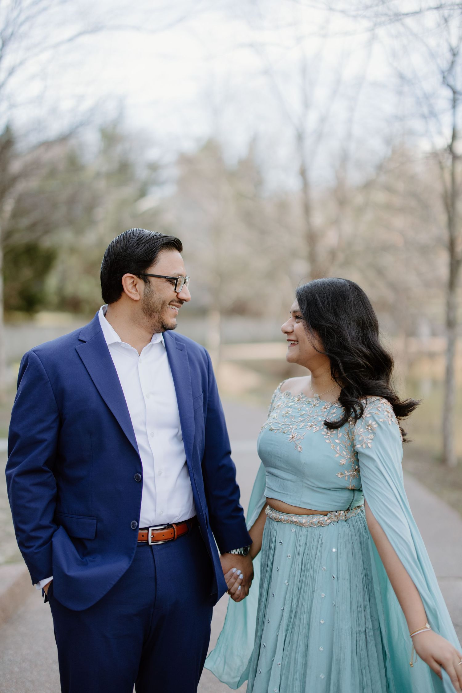A couple in formal attire, with him in a navy suit and her in a flowing mint green dress, share a joyful moment outdoors.