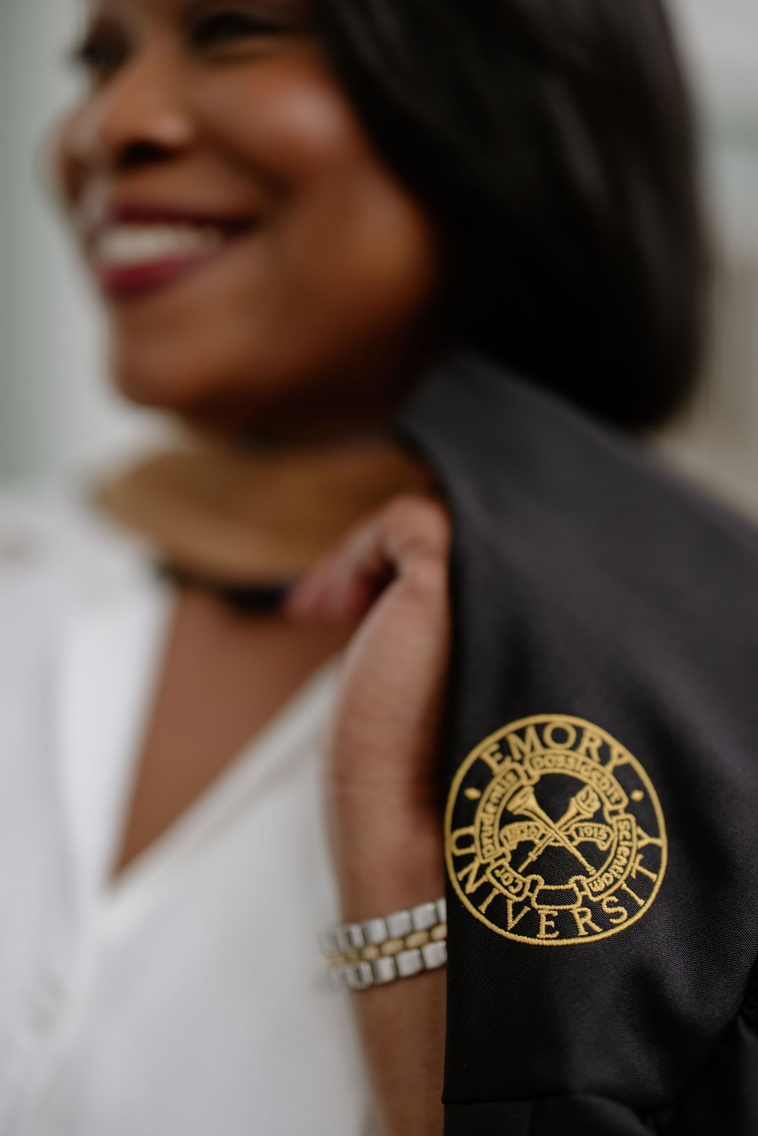 Smiling woman holding an Emory University black graduation gown with gold emblem logo on the shoulder.