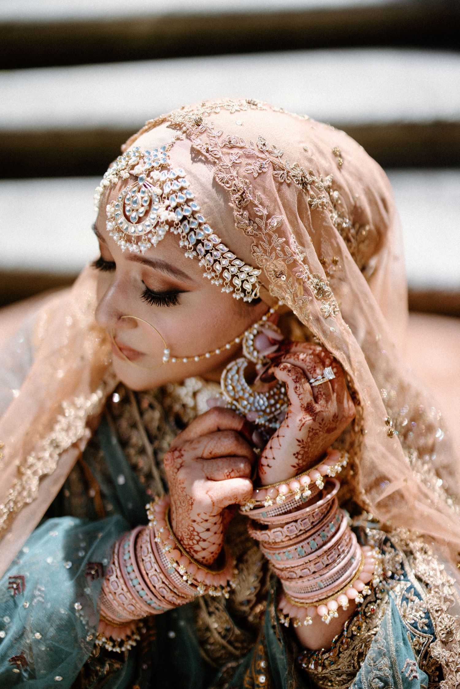 A bride adorned in intricate jewelry and beige veil displays traditional South Asian bridal fashion.