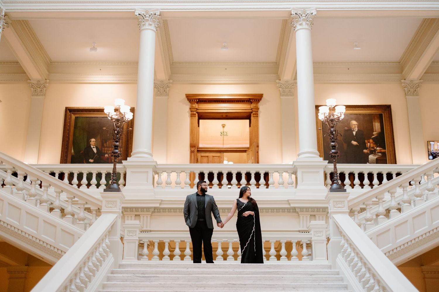 People stand on an ornate white marble staircase in formal attire during an event at an elegant venue.
