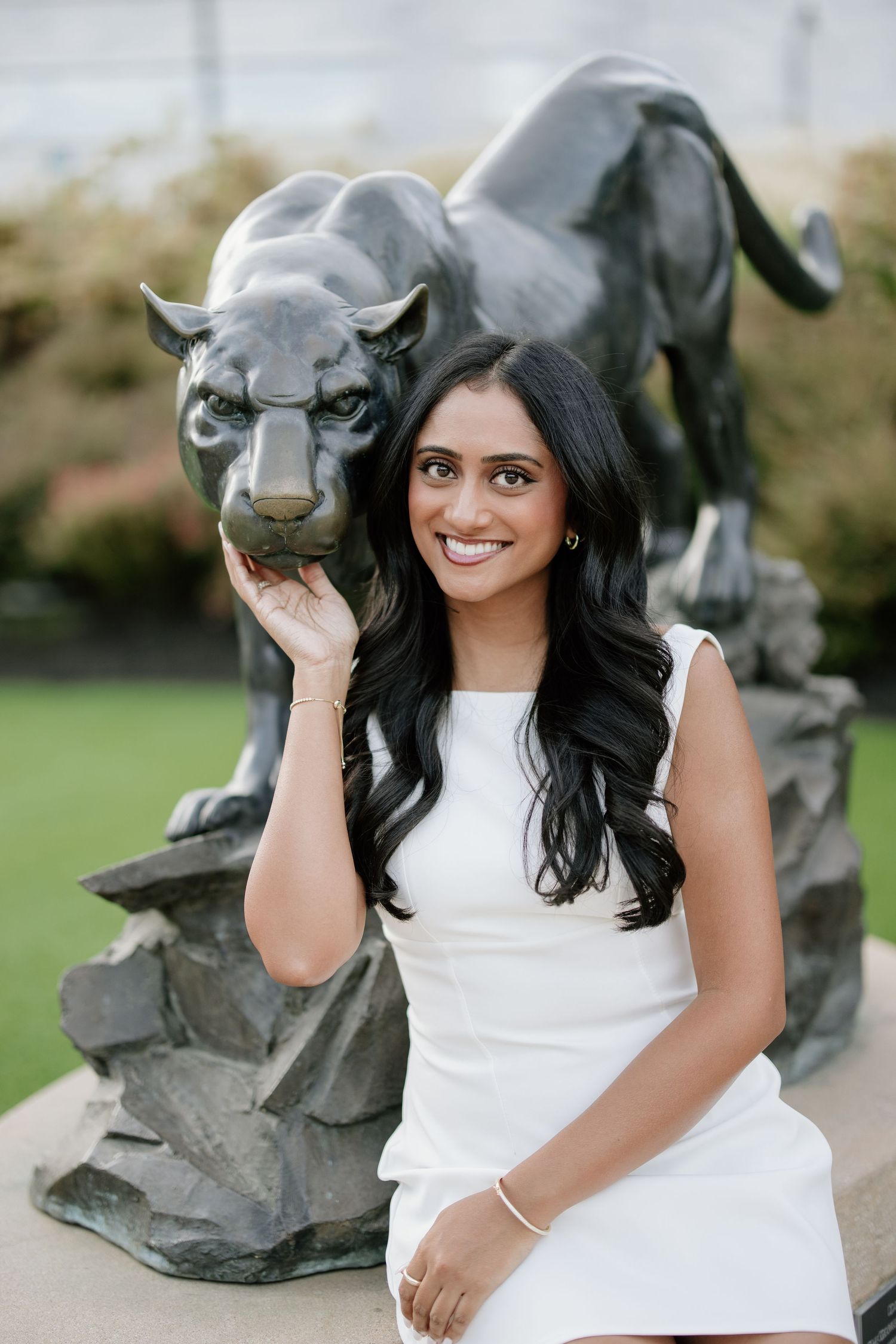 Young woman in white dress posing beside a black panther statue outdoors, smiling at the camera.