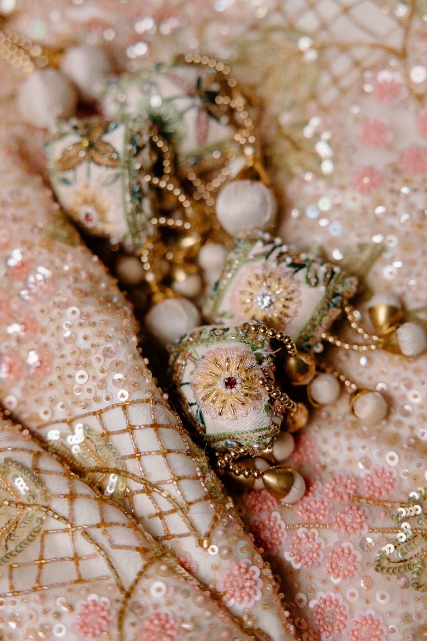 Close-up detail of intricate gold embroidery and glitter on pink and white fabric with delicate patterns.