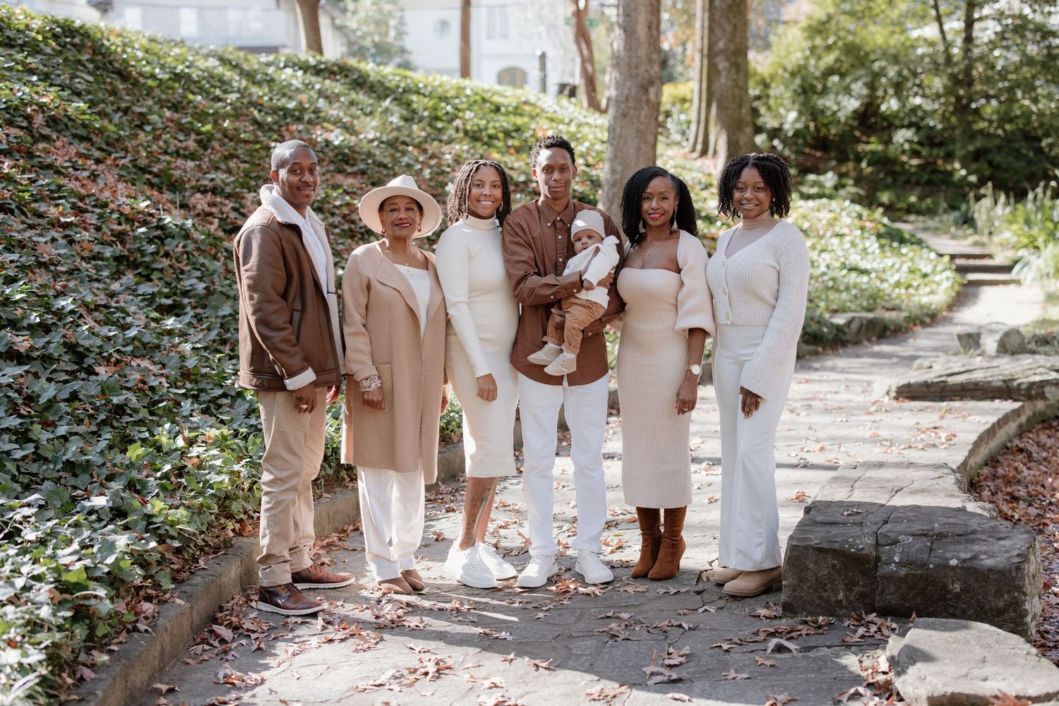 A group in coordinated neutral outfits poses together on a garden path surrounded by lush greenery.