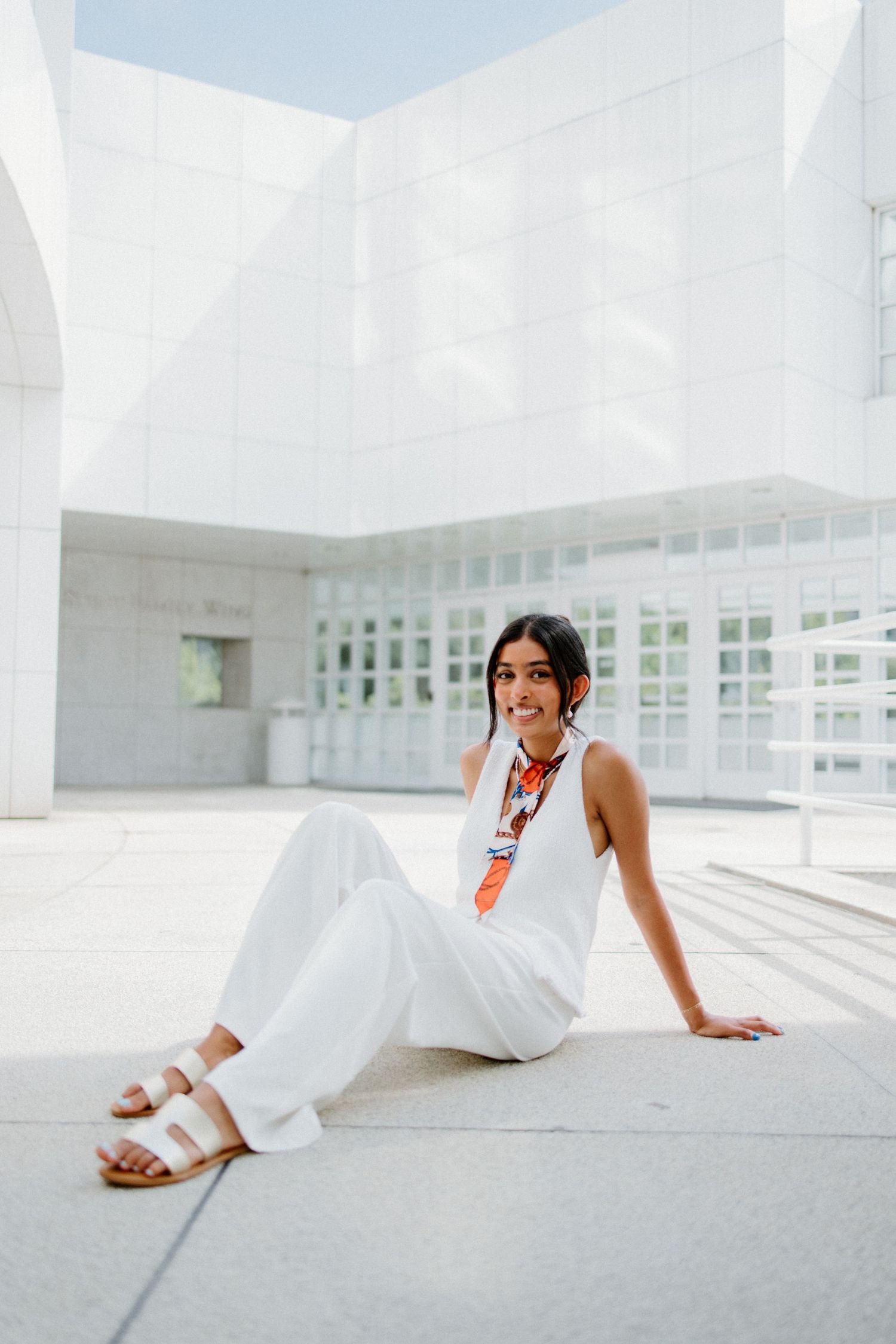 Person in white outfit sitting on modern minimalist white architectural space with clean angles and lines.