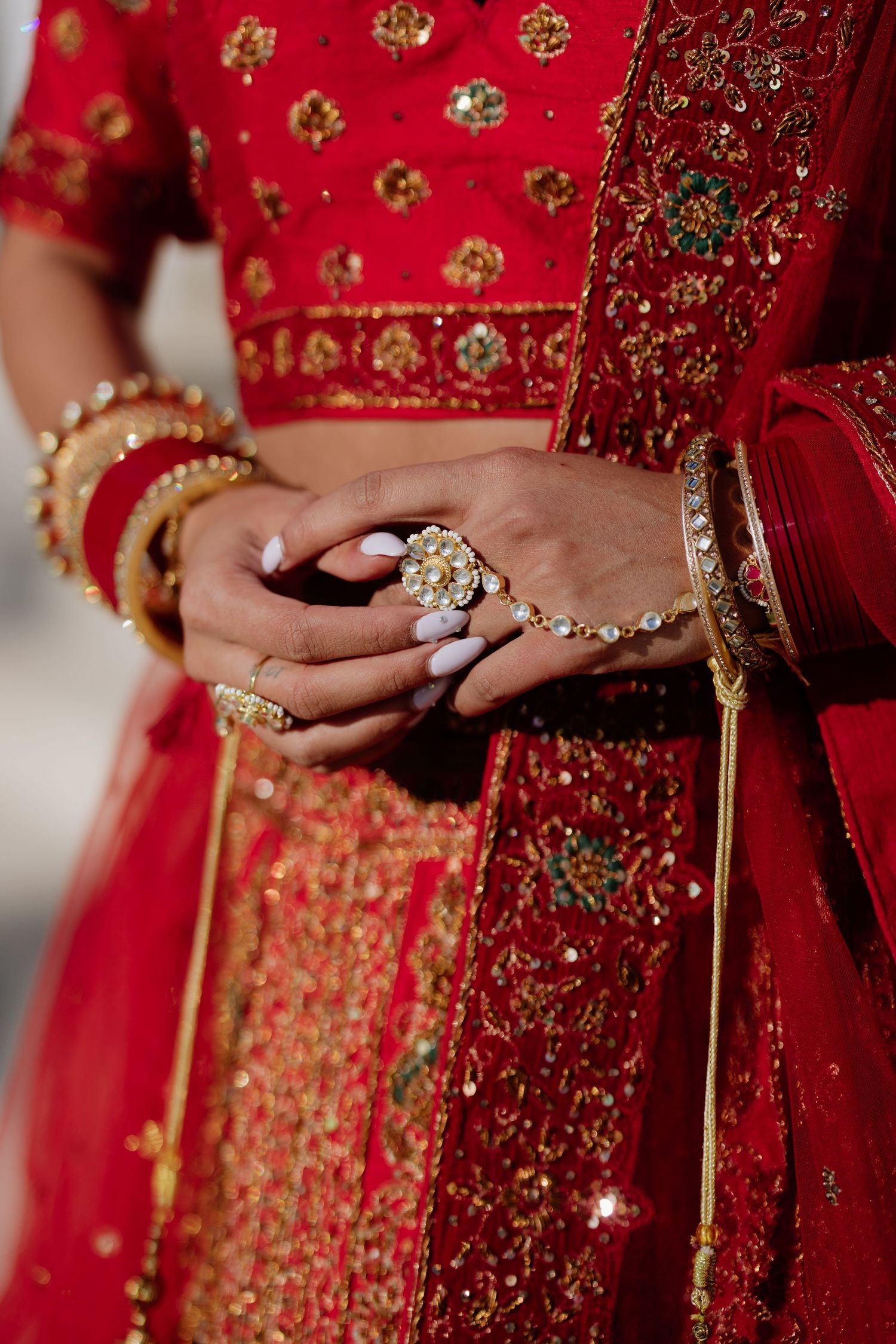 Close-up details of traditional Indian bridal attire showing red and gold embroidered fabric and jewelry details.