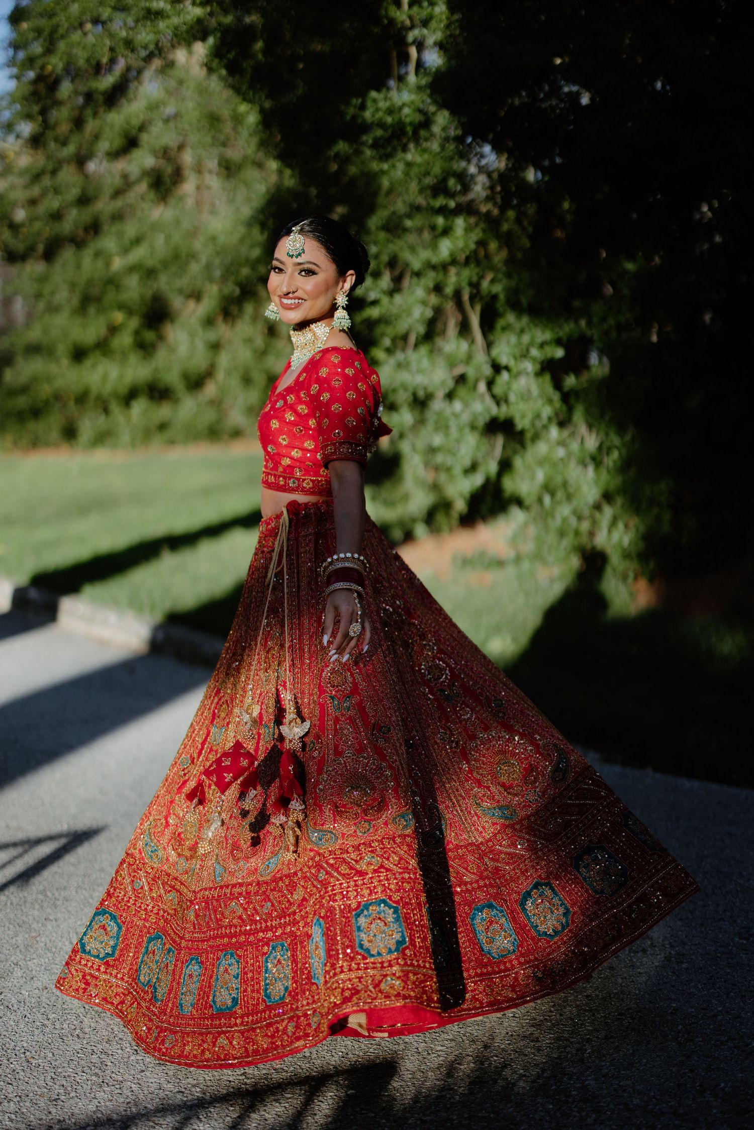 Traditional Indian bridal lehenga in vibrant red with intricate embroidery and blue details twirls elegantly against nature backdrop.