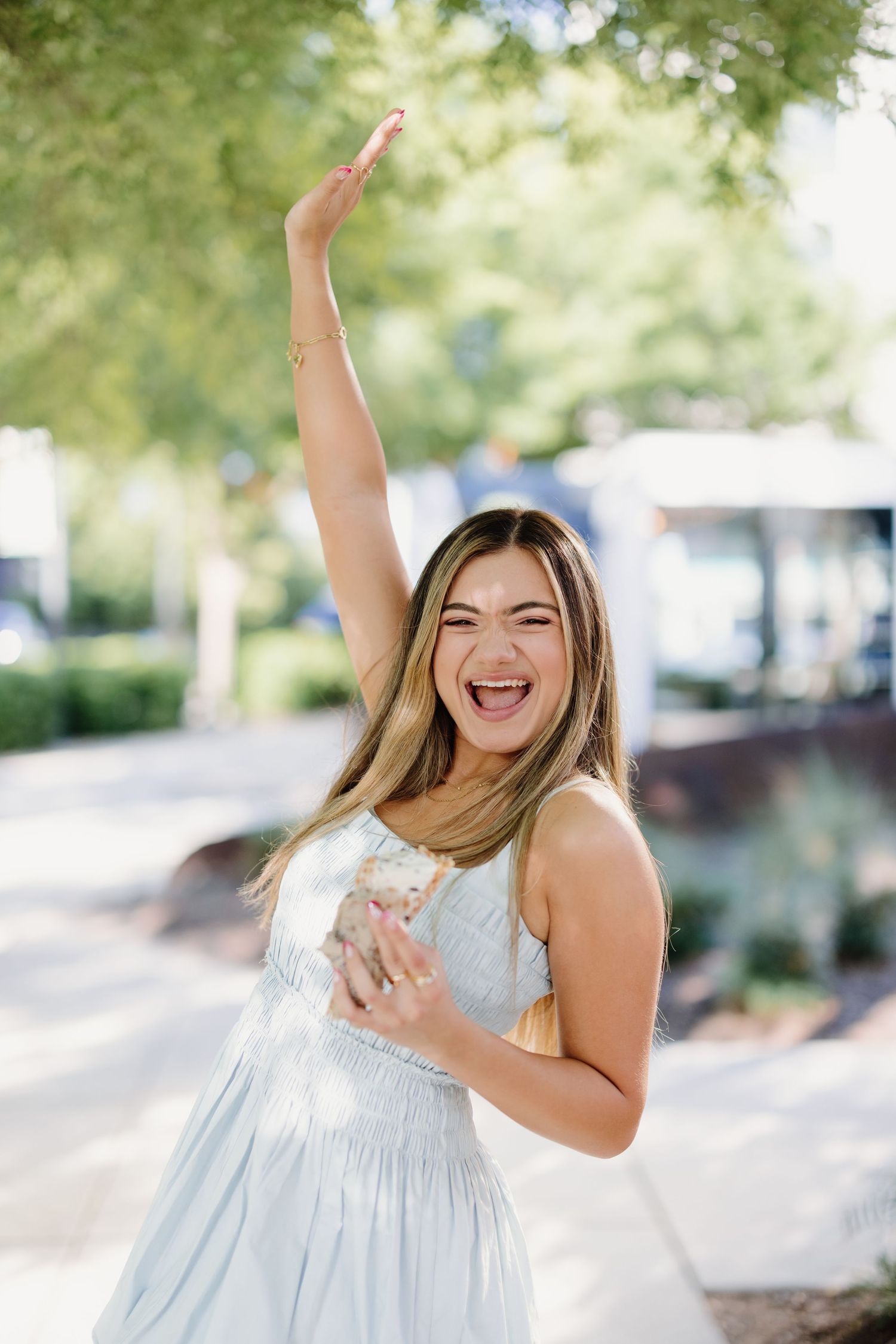 A joyful moment captured outdoors in a white sundress with one arm raised in celebration.