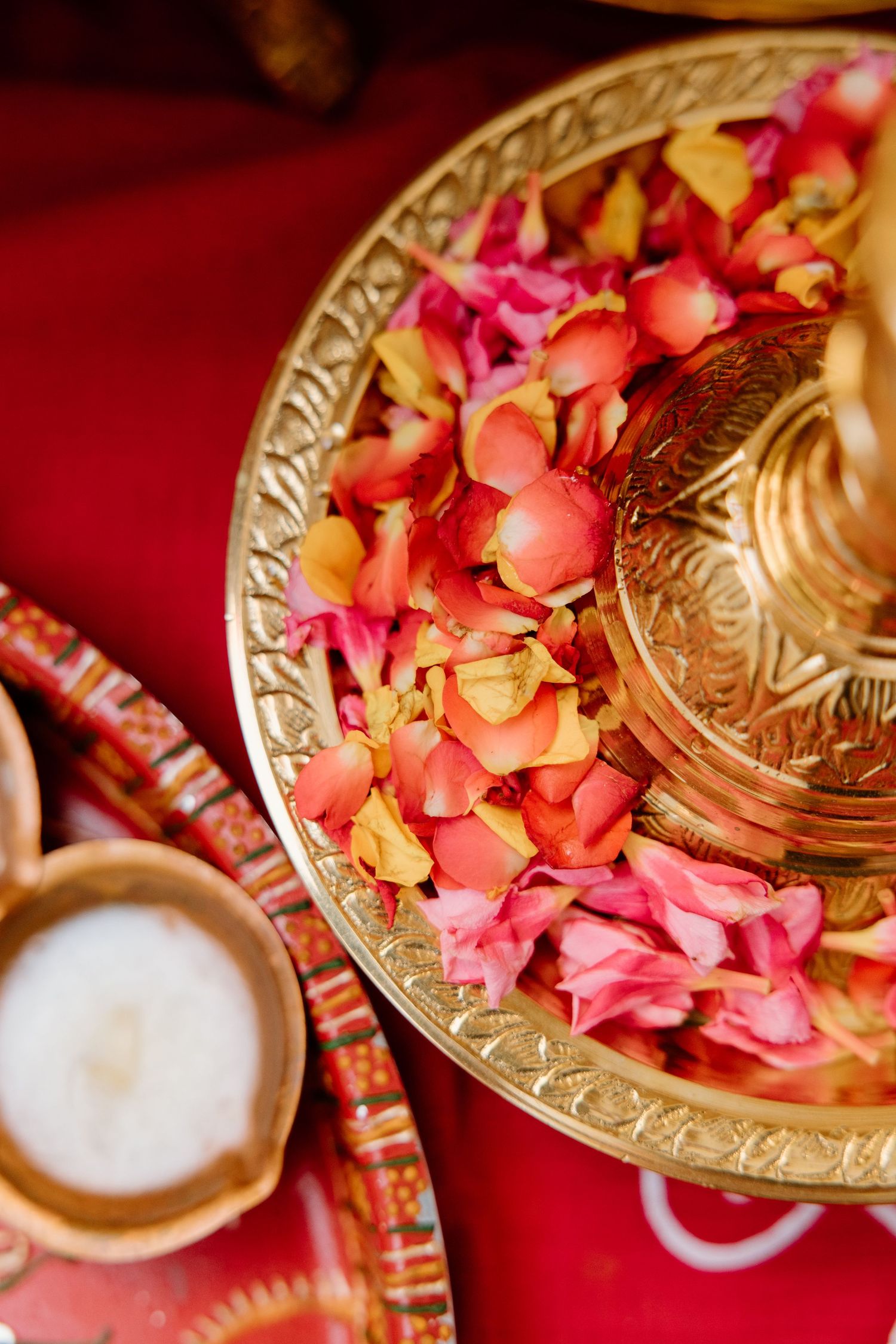 Pink and orange rose petals scattered on ornate gold plates with frosted glass tealight holders creating a romantic table setting.