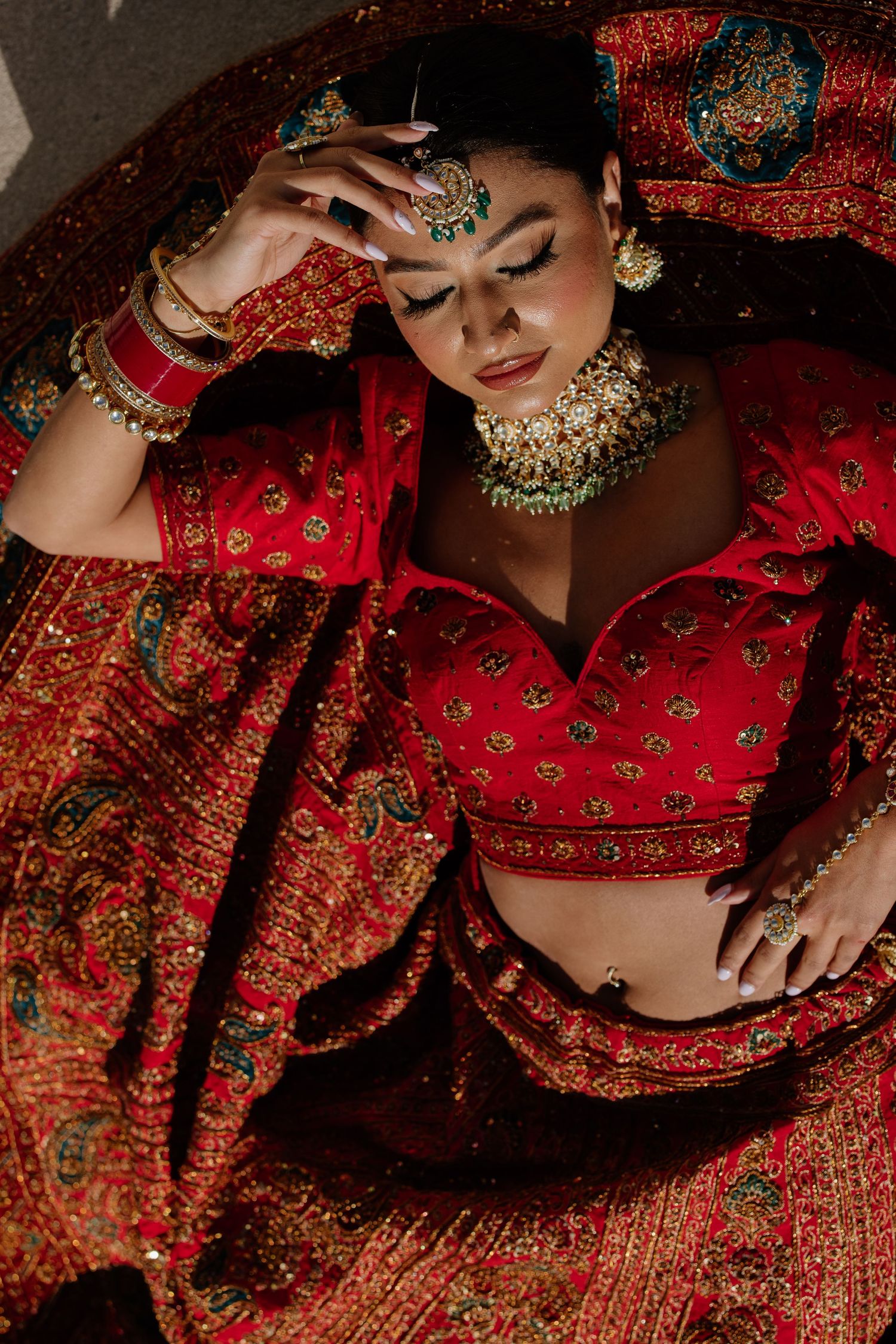 Close-up details of ornate traditional Indian bridal attire in rich red and gold with intricate embroidery and jewelry.