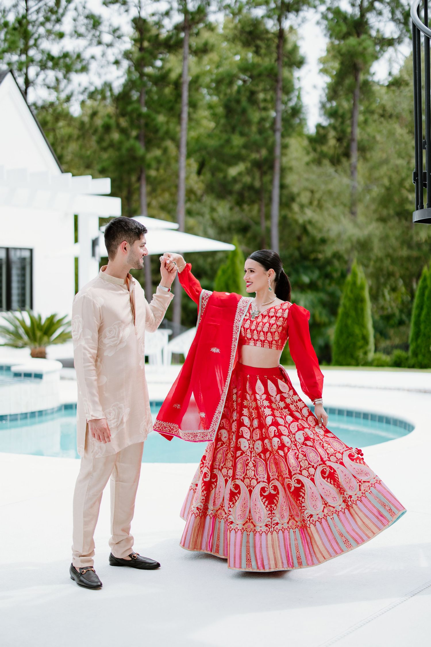 Two people dance together by a pool wearing complementary beige and red formal attire.