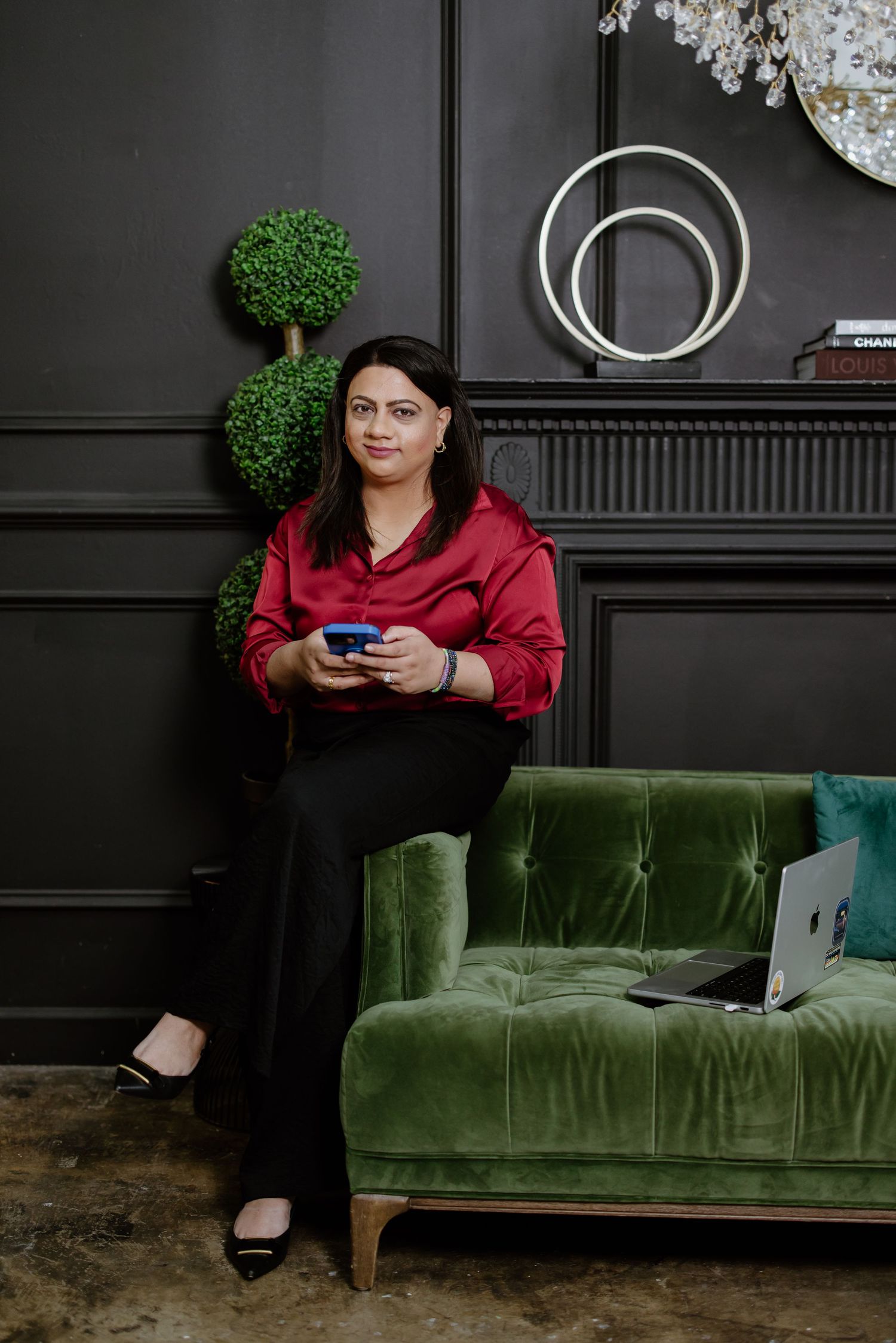 Someone sits comfortably on a green velvet couch against a dark wall with modern decor, holding a phone.