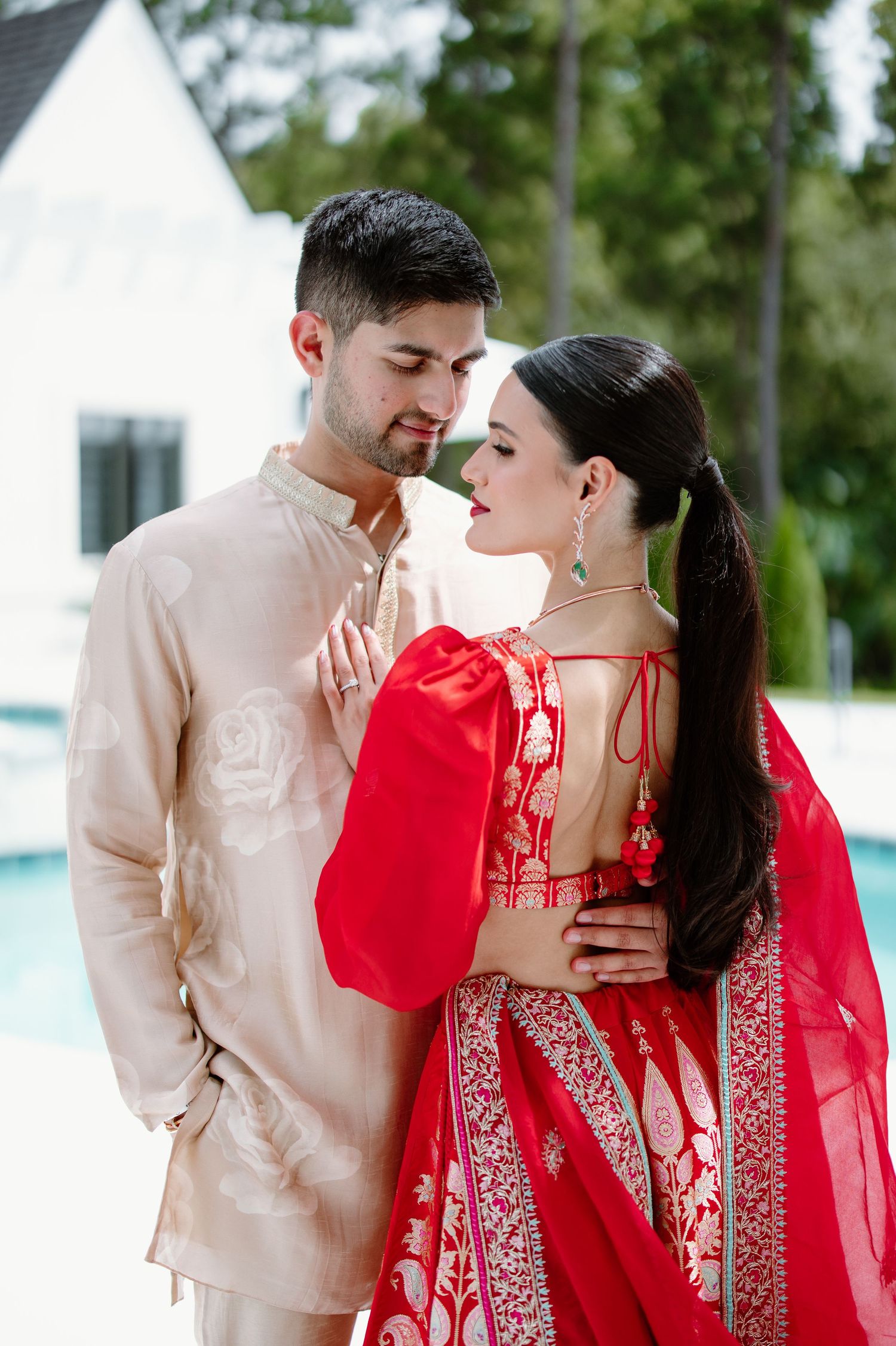 A couple embraces while wearing traditional South Asian attire in beige and red colors.