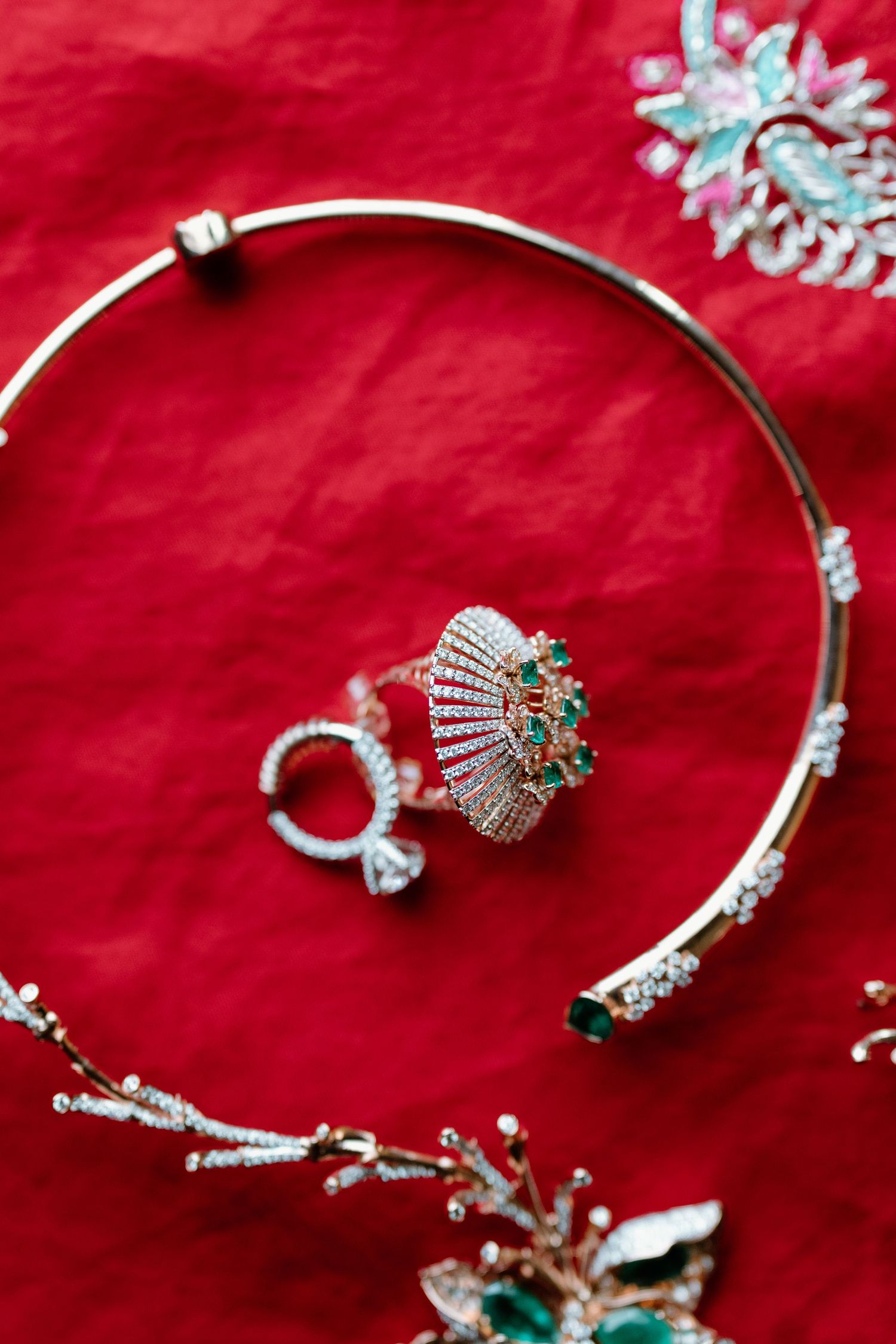 Elegant jewelry set with emerald green stones and silver details displayed on red fabric.