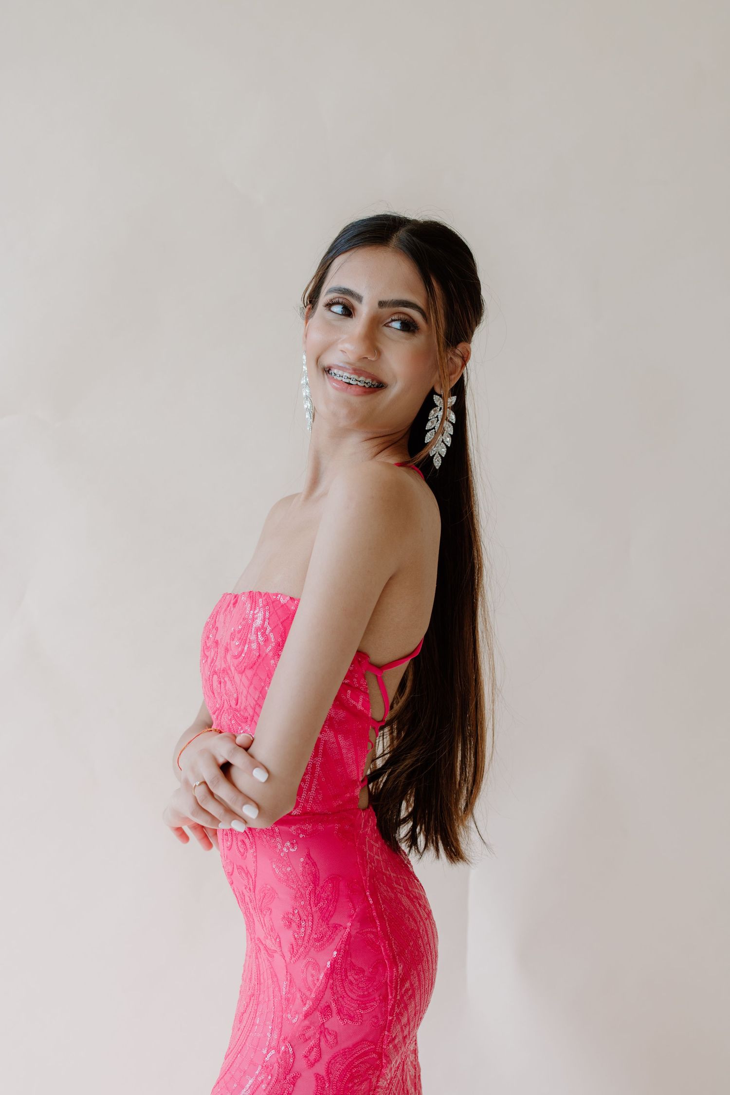 Person wearing a bright pink lace dress poses playfully against a light colored wall background.
