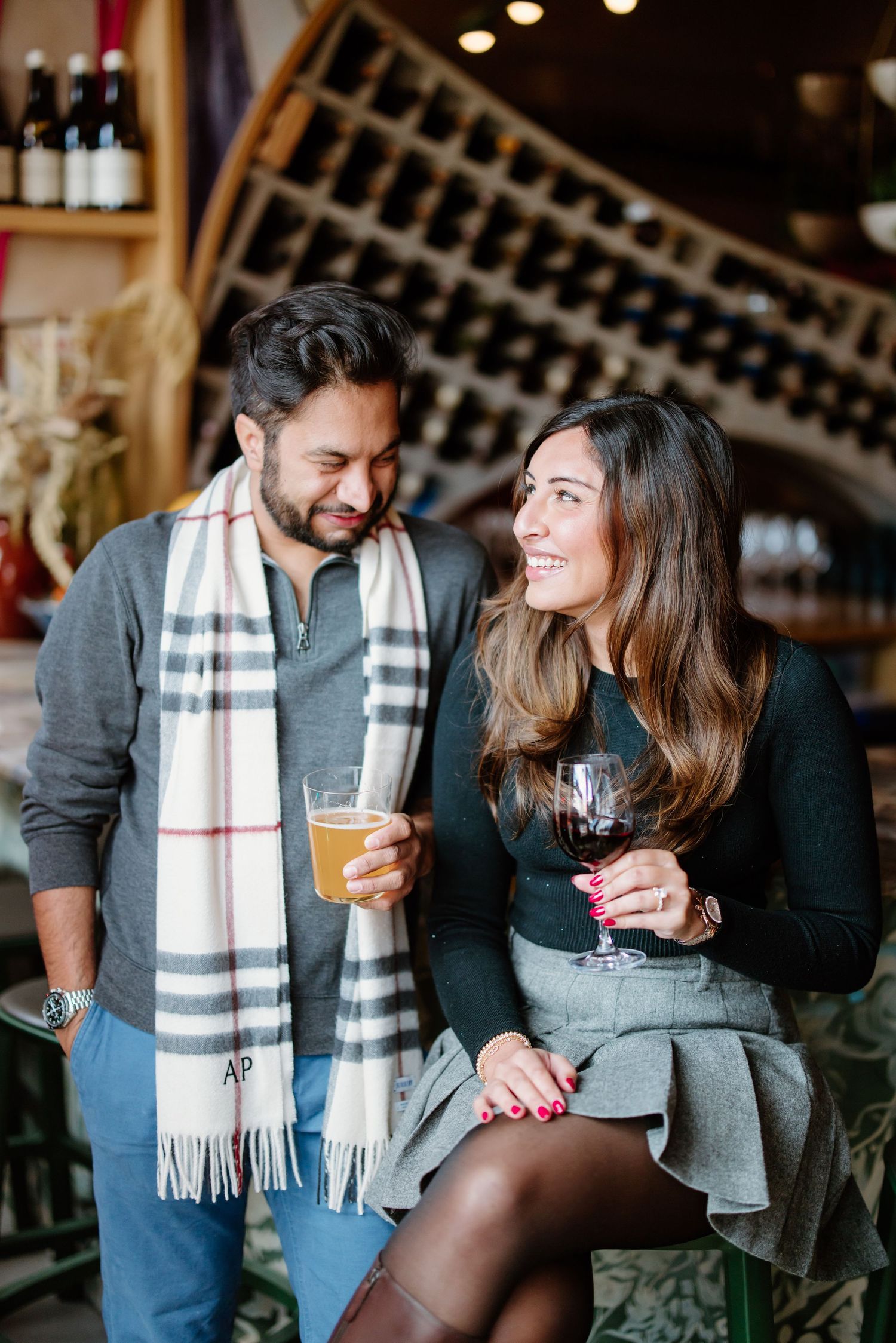 A couple enjoying drinks together at a wine bar, with a wine rack display visible in the background.