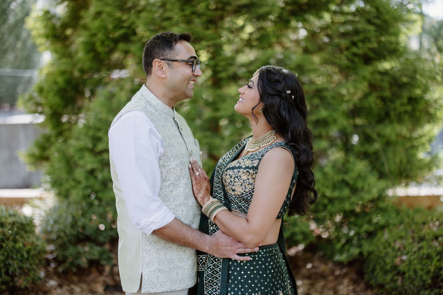 A couple stands together outdoors sharing an intimate moment against a green leafy background.