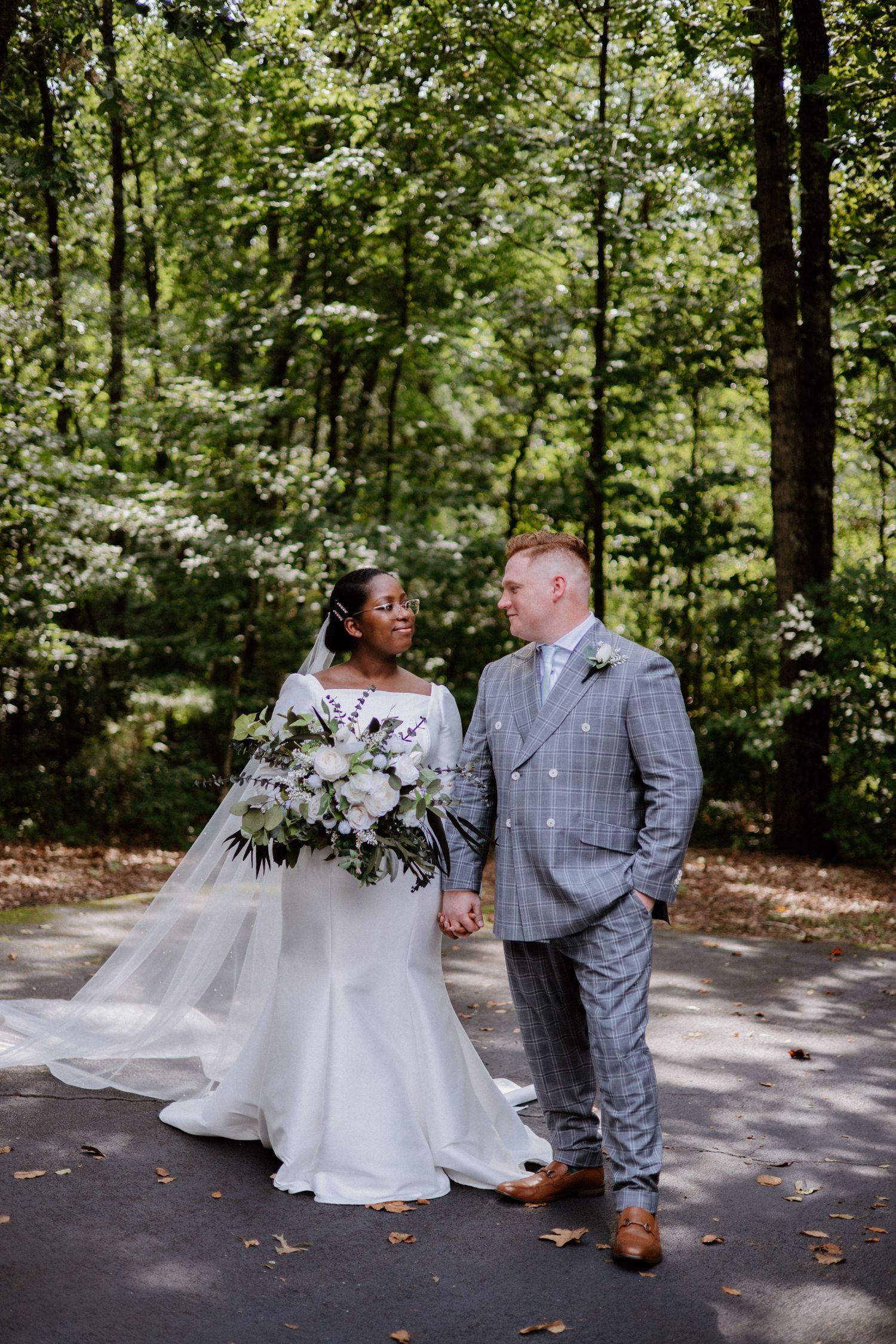 A couple shares romantic moments in four sequential wedding photos taken on a wooded path surrounded by greenery.