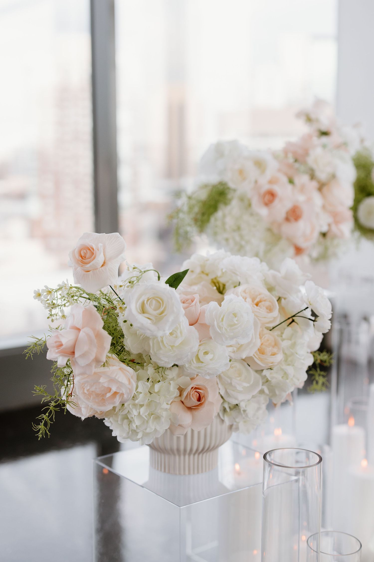 Elegant floral centerpiece arrangements with blush pink and white roses in modern white ribbed vases on a sleek surface.