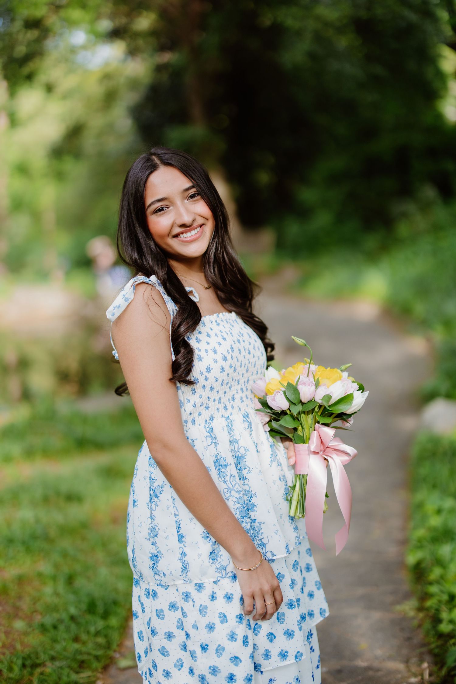 Someone in a blue and white floral summer dress holds a bouquet of tulips while standing on a garden path.