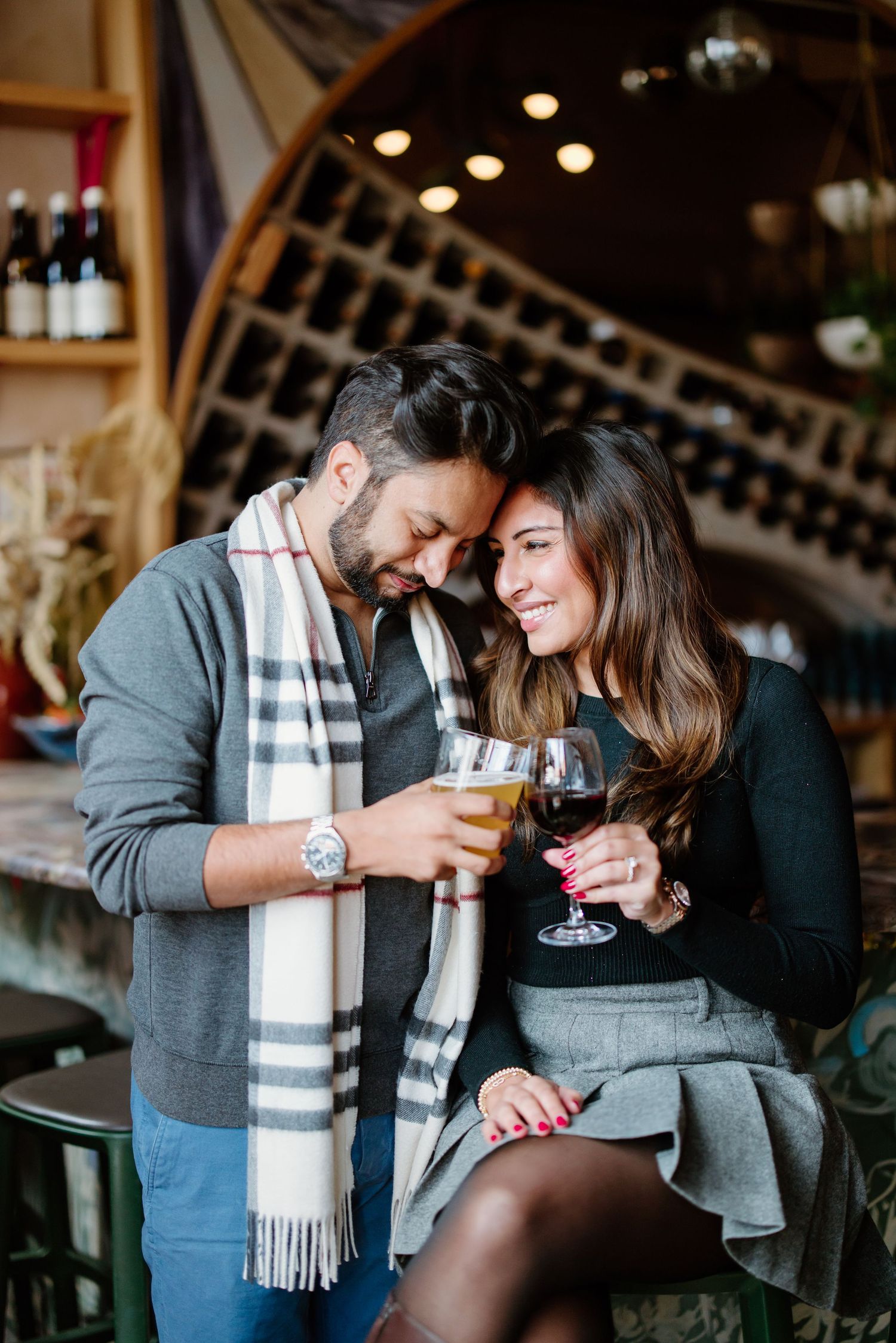 A couple shares wine and laughter in a cozy wine cellar setting.