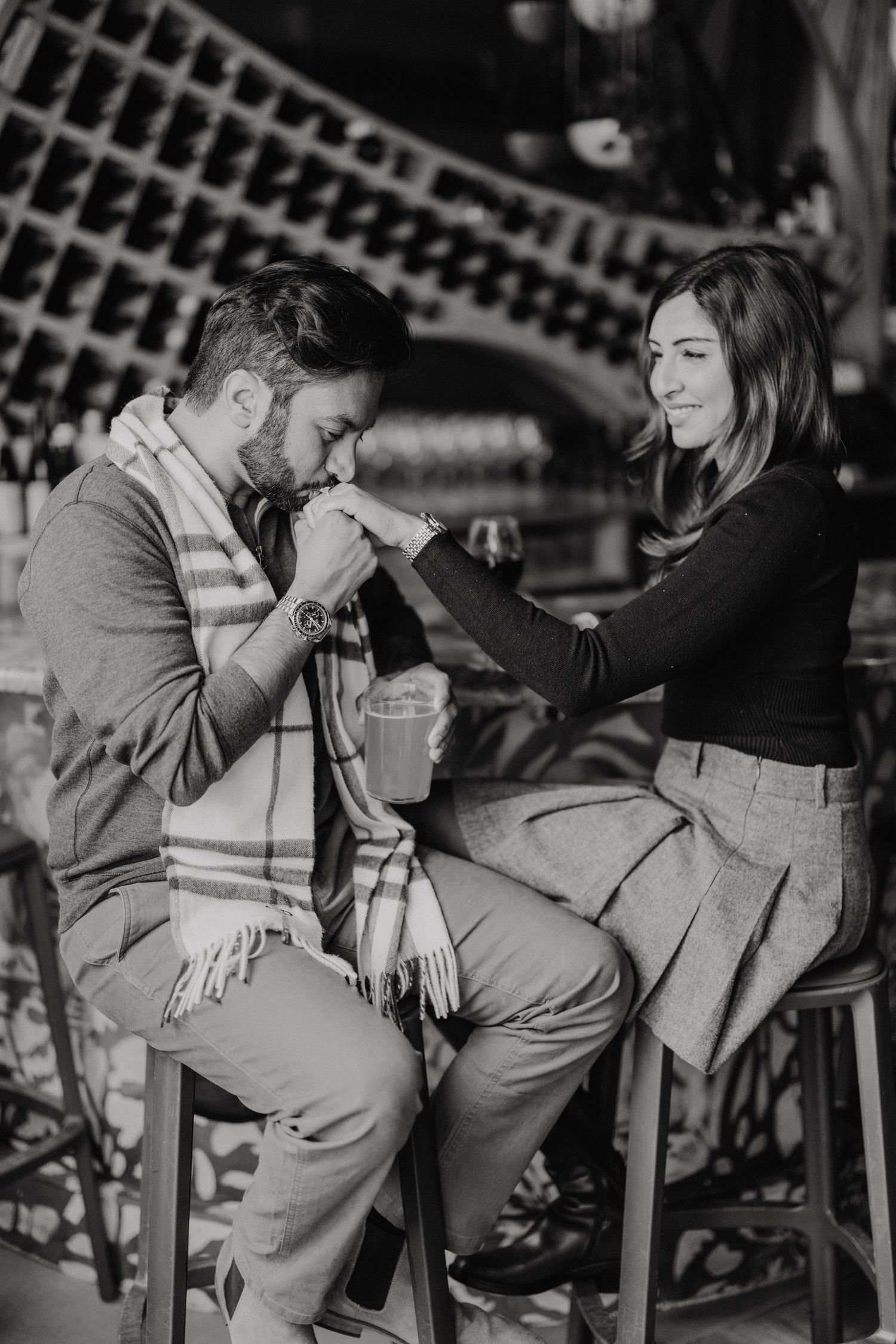 A romantic black and white photo showing a tender moment between a couple sitting on chairs at a cafe.