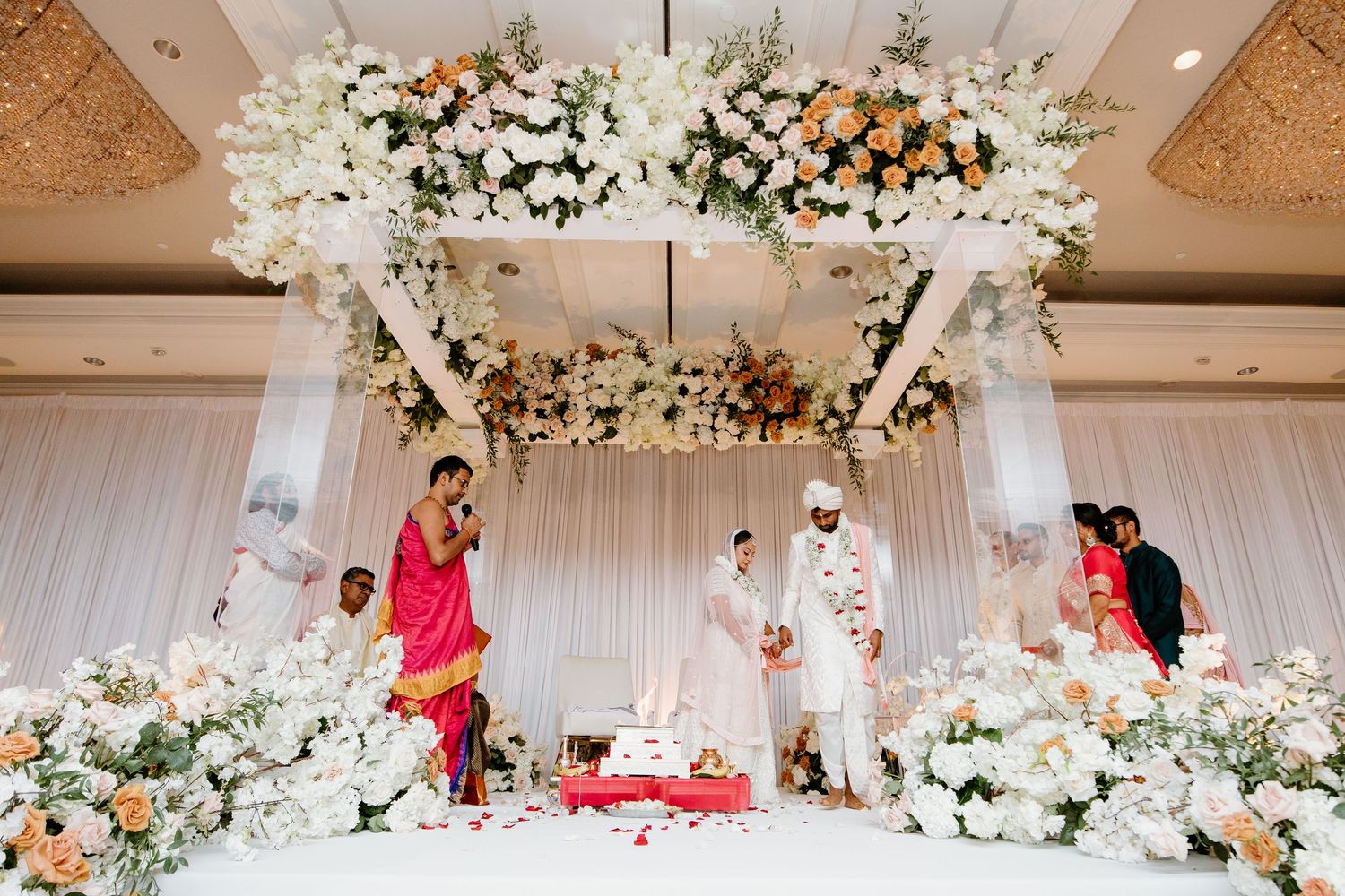 A panoramic view of an elegant white and gold wedding reception venue with floral chandeliers and romantic lighting.