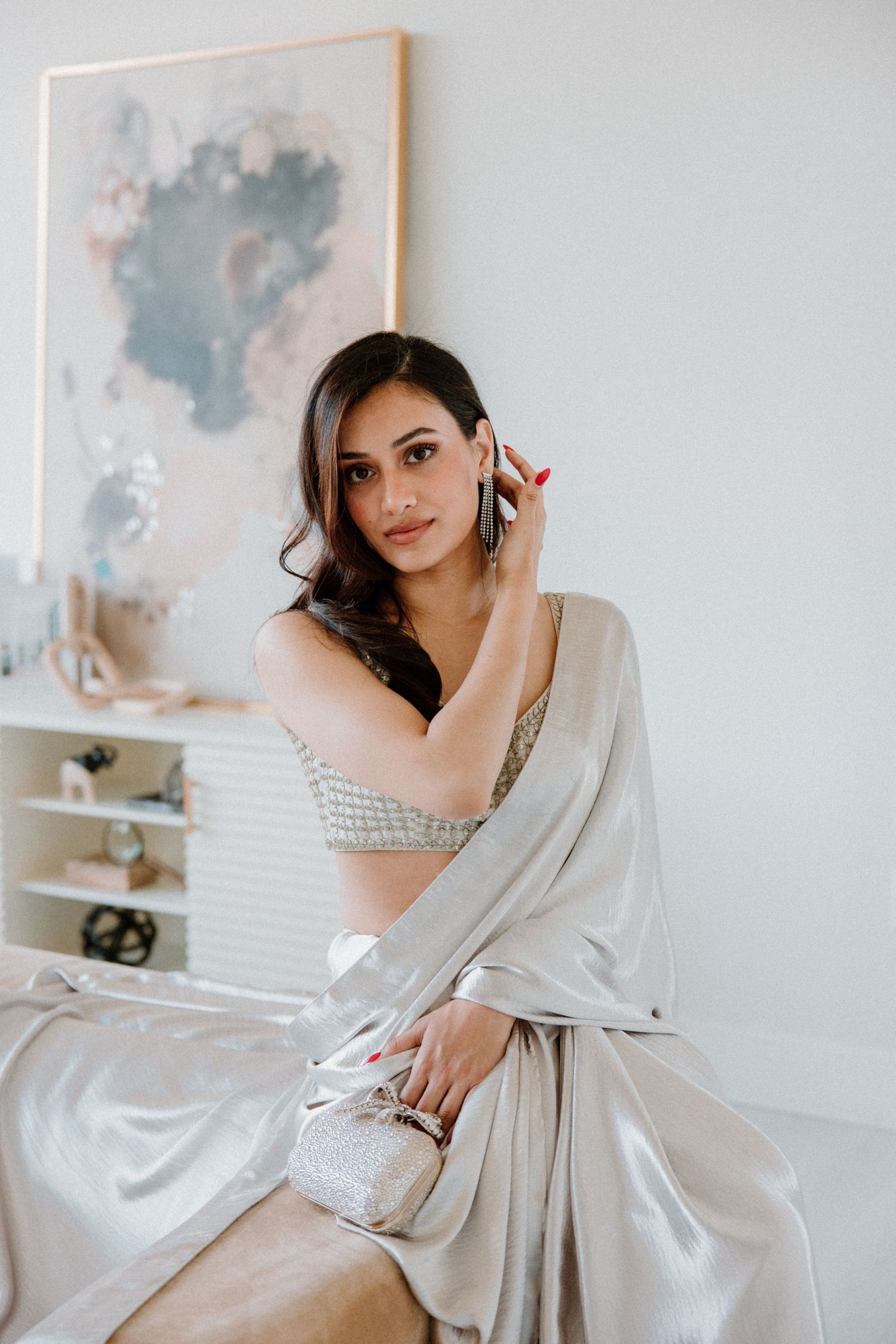 Elegant portrait in a light-filled room with pale grey sari and abstract artwork on the wall in soft blue tones.