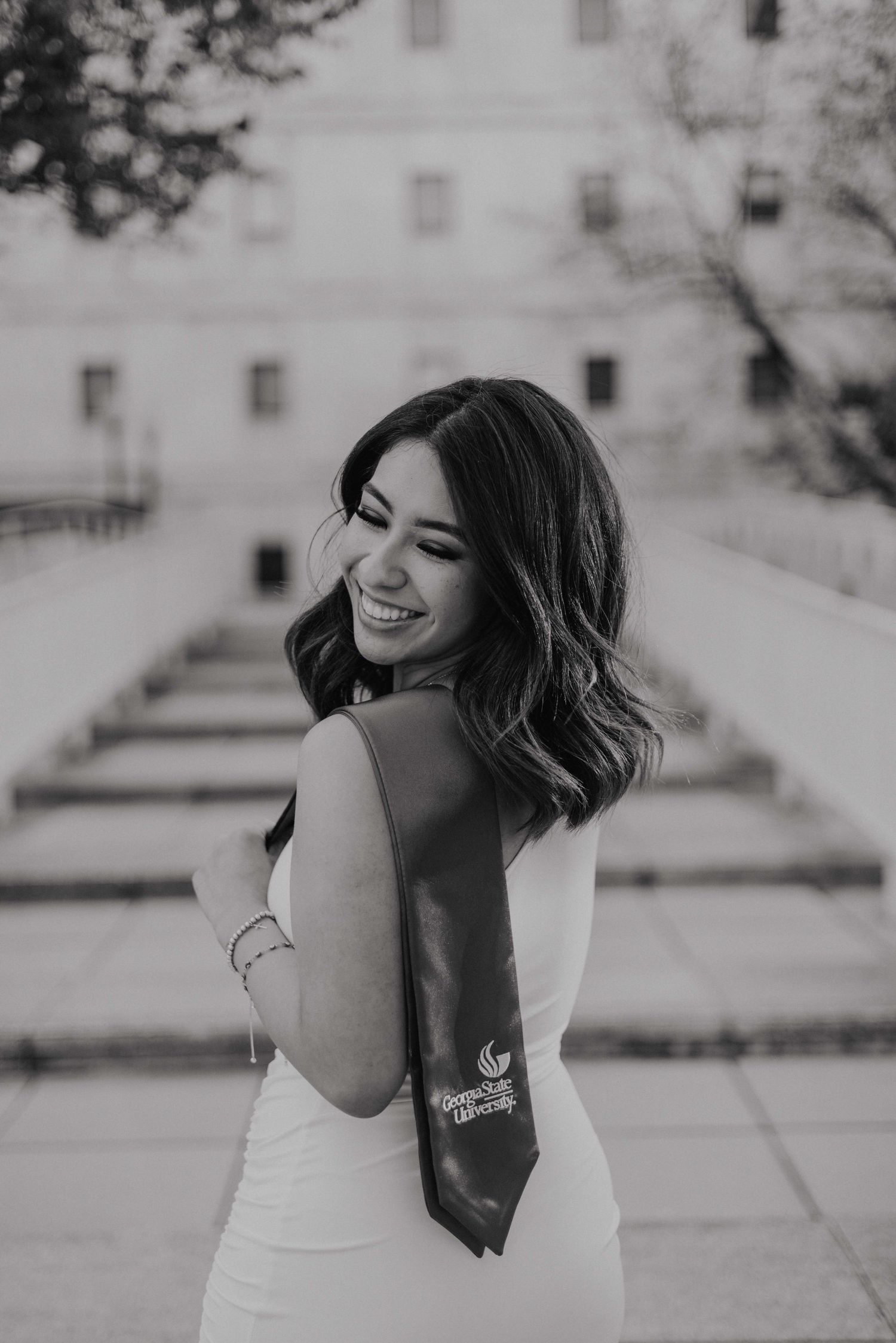 Black and white portrait of someone in a white dress smiling over their shoulder on outdoor steps.