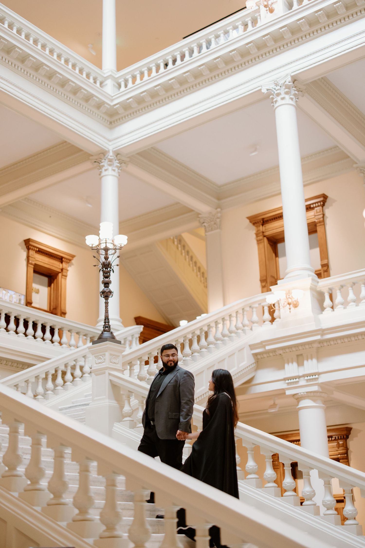 Elegant marble staircase with ornate white columns and balustrade in a classical interior, with warm lighting and cream walls.