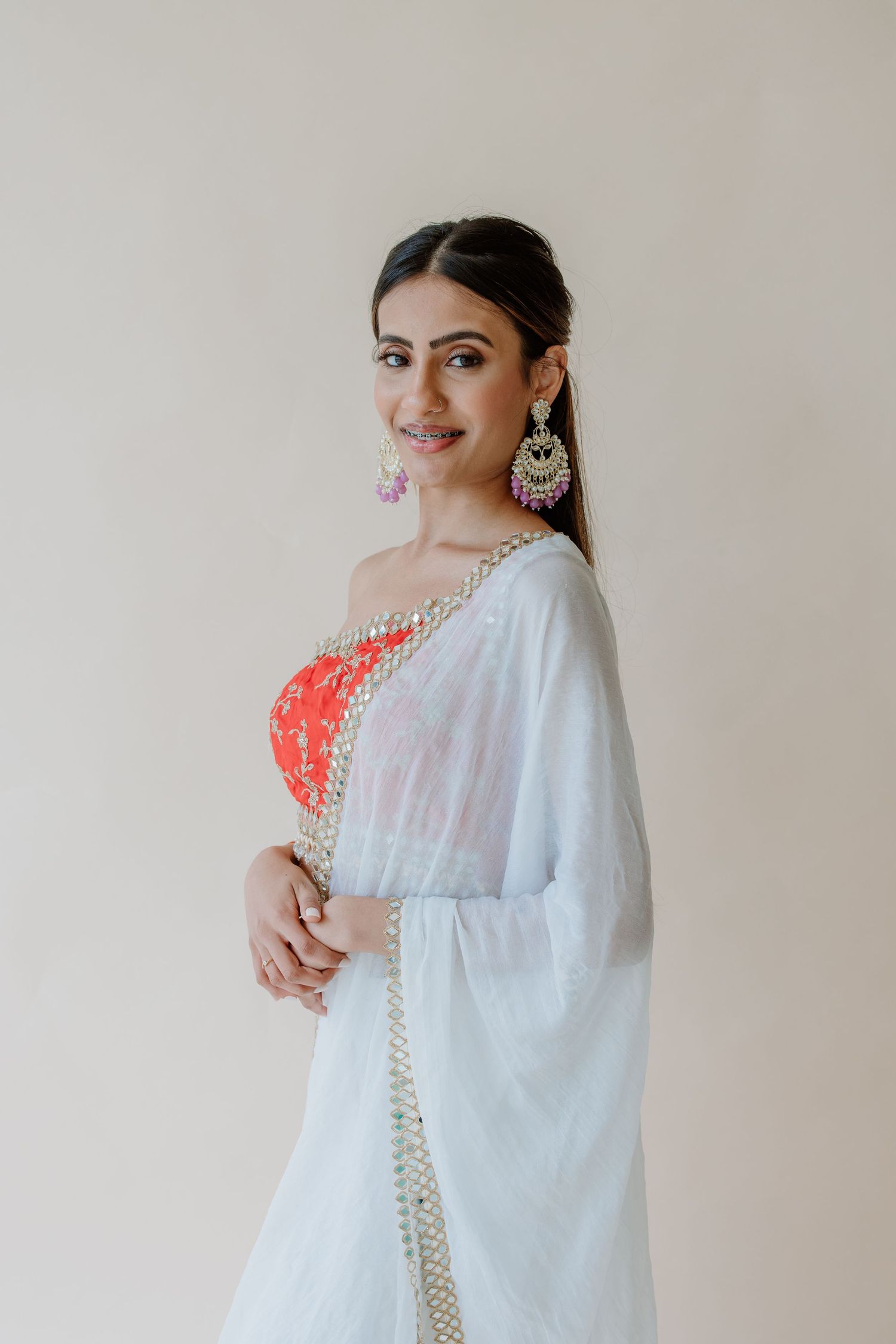 A series of poses in traditional white ethnic wear with statement jewelry against a neutral backdrop.