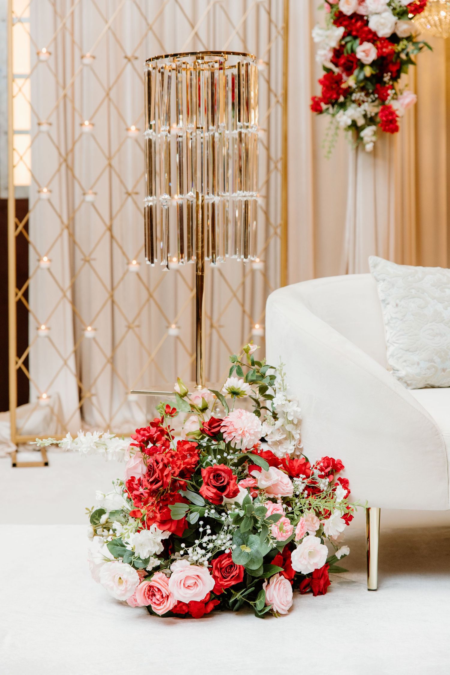 Elegant wedding decor features crystal chandeliers and floral arrangements with red and white roses against a gold patterned wall.