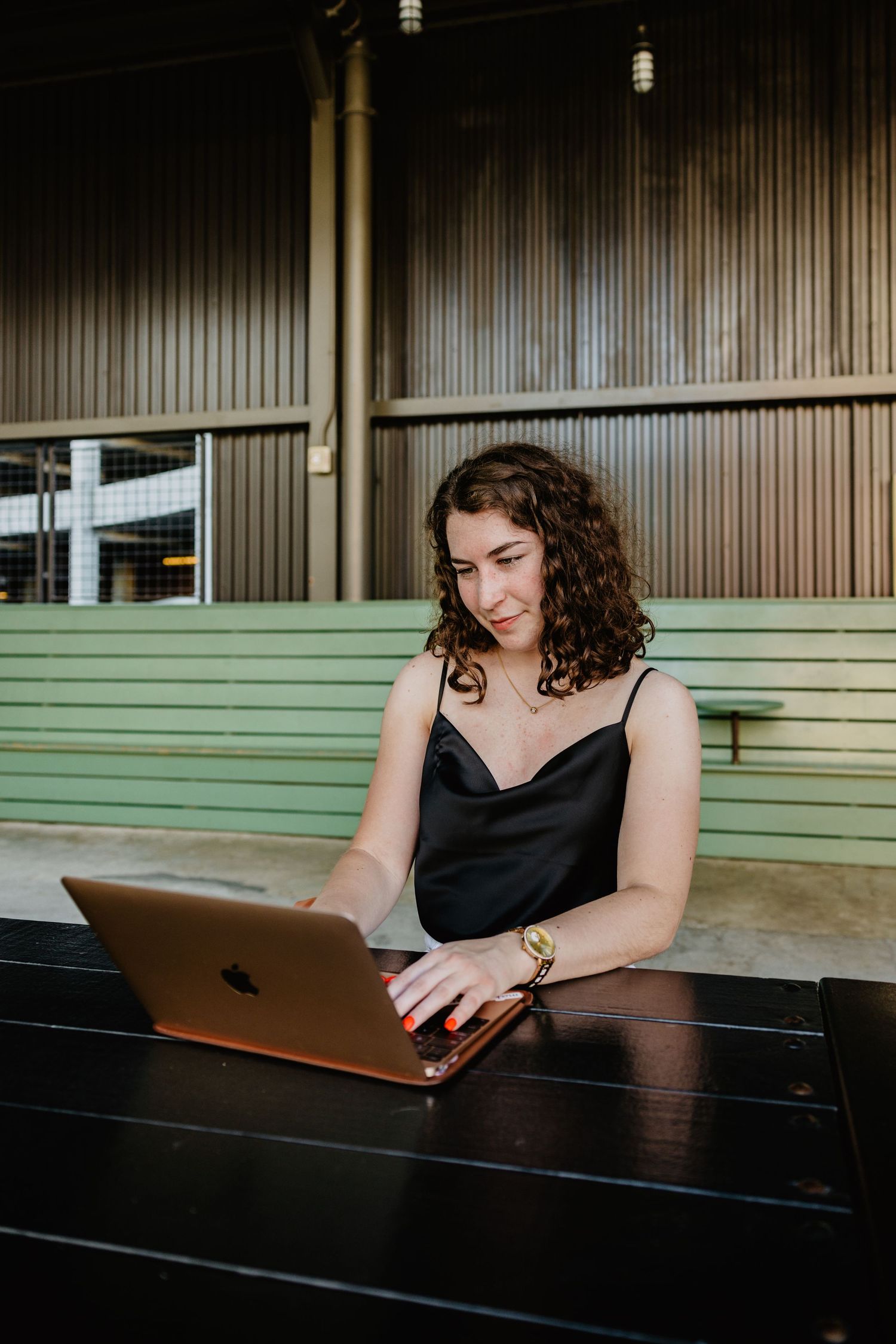 Professional working on MacBook laptop at wooden table in casual setting with sage green bench seating.