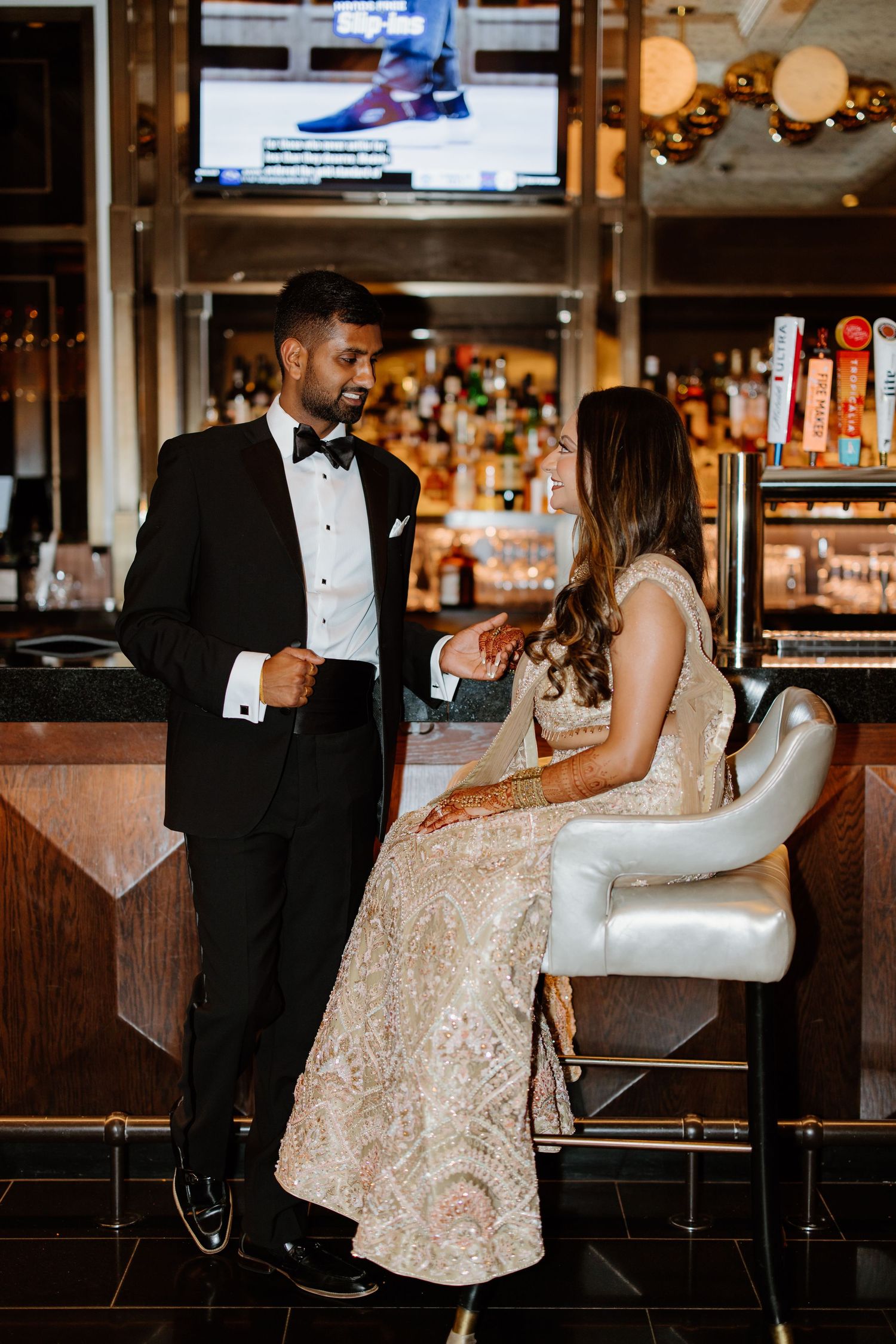 Elegantly dressed couple in formal attire having drinks at an upscale bar with ambient lighting.