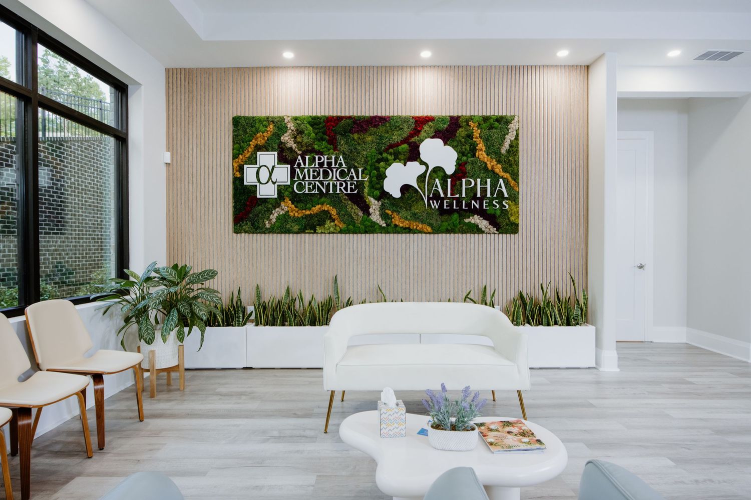 Modern spa waiting room featuring a moss wall with white floral logo, white furniture and indoor plants.