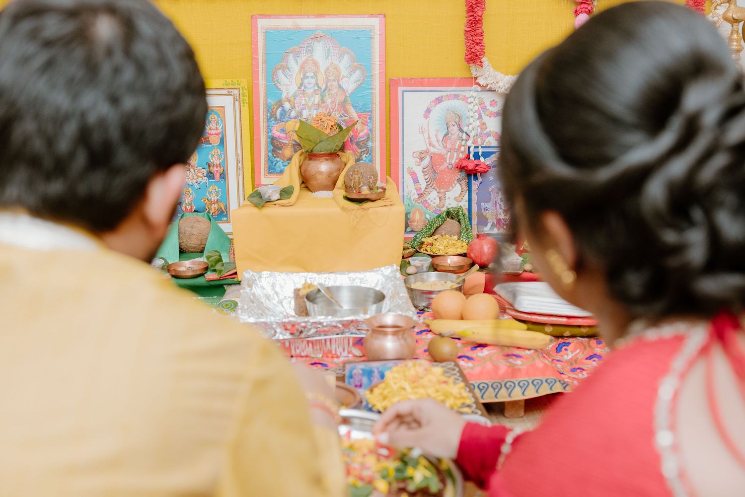 Two people sit before a colorful altar with religious icons and decorative elements during a ceremony.