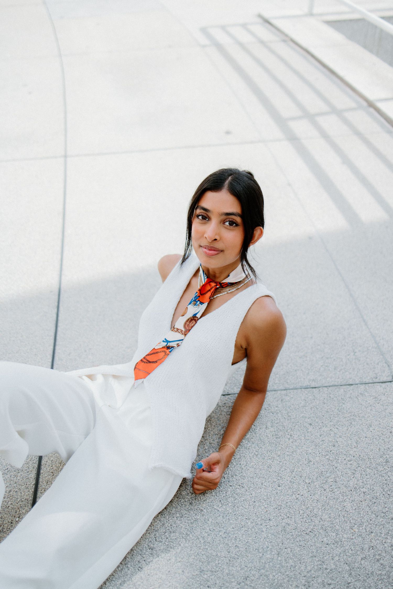 Elegant white jumpsuit paired with colorful silk scarf for a modern minimalist summer look on concrete backdrop.