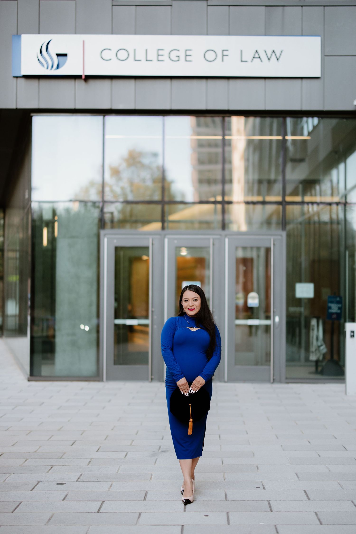A person in a blue dress stands outside a College of Law building entrance.