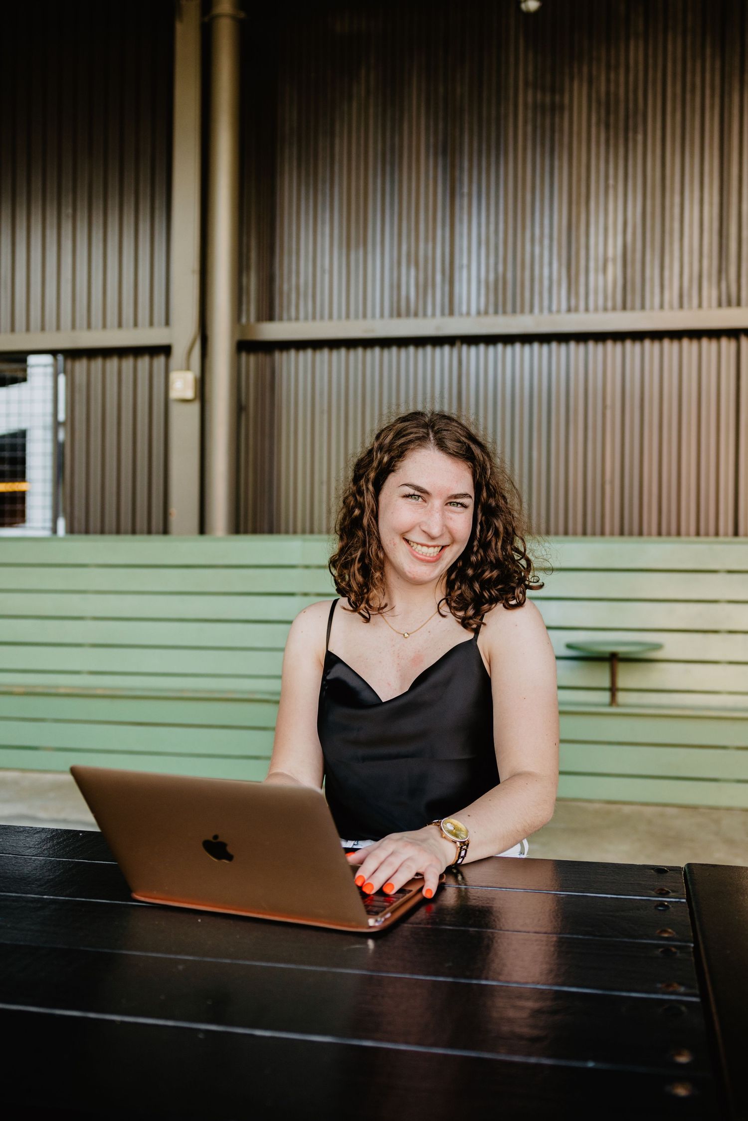 Professional working with MacBook laptop at dark wood desk wearing a black sleeveless top.