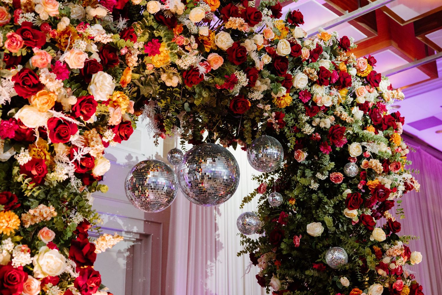 Elegant floral arch with pink and red roses adorned with hanging crystal chandeliers creates a luxurious wedding backdrop.