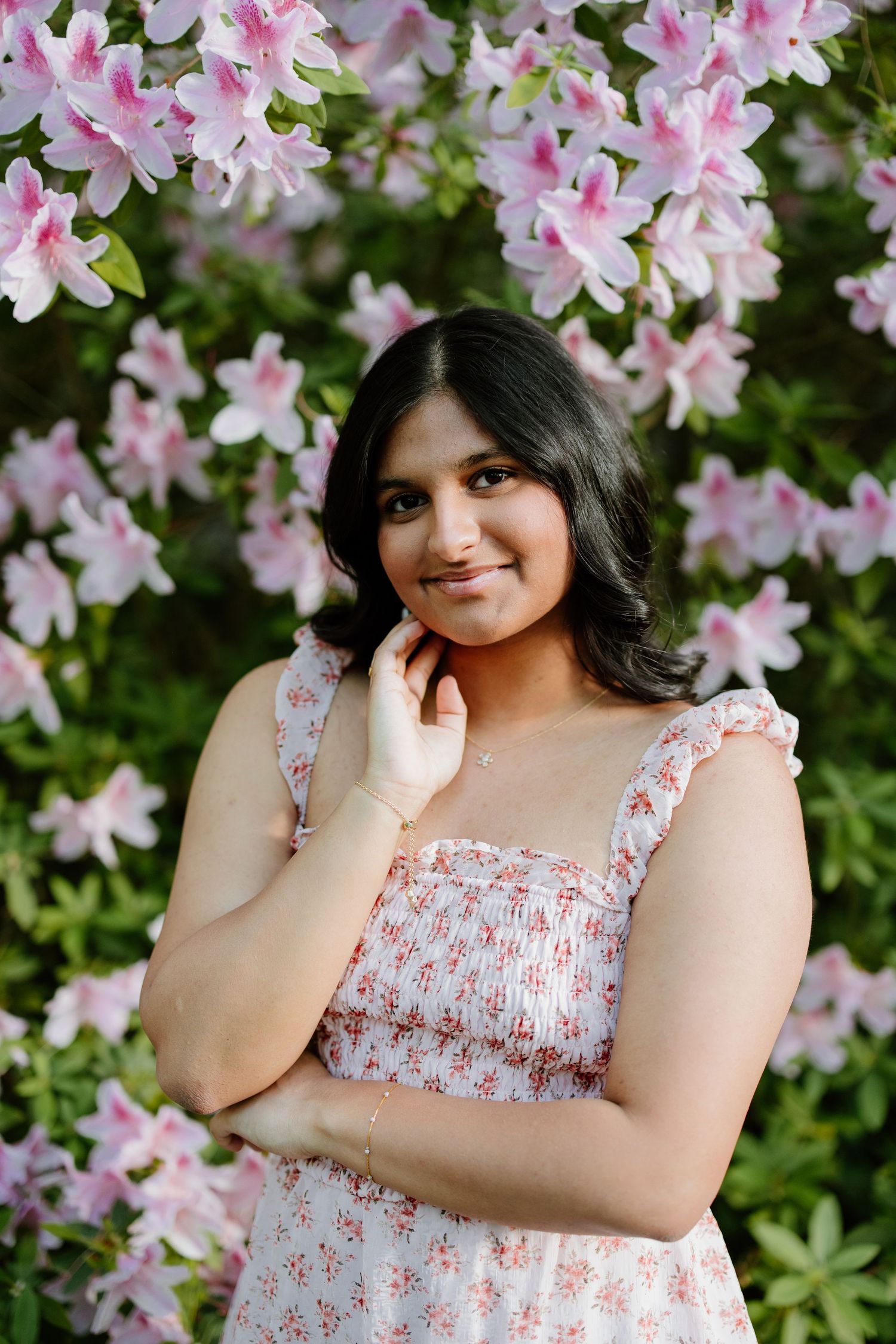 A portrait taken in front of blooming pink azalea flowers while wearing a floral patterned dress.