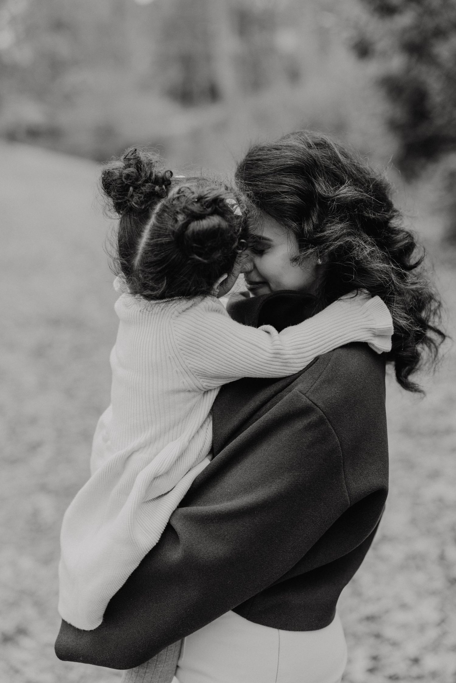 Two people embrace in a tender black and white moment as windswept hair frames their intimate interaction.
