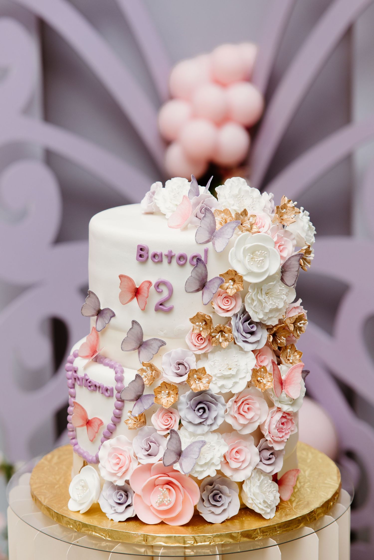 A beautiful white and pink wedding cake decorated with delicate floral arrangements and gold accents shown from multiple angles.